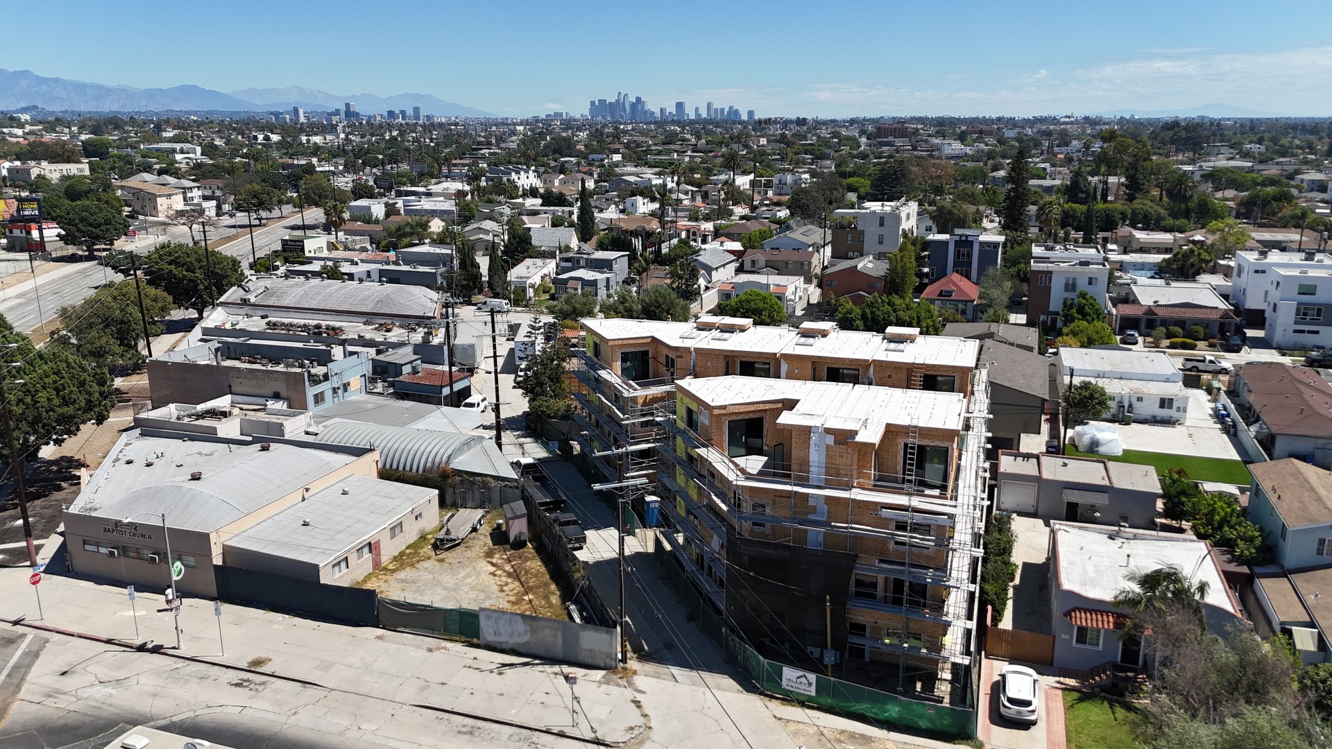 Aerial view of a multifamily building under construction with the downtown Los Angeles skyline beyond.