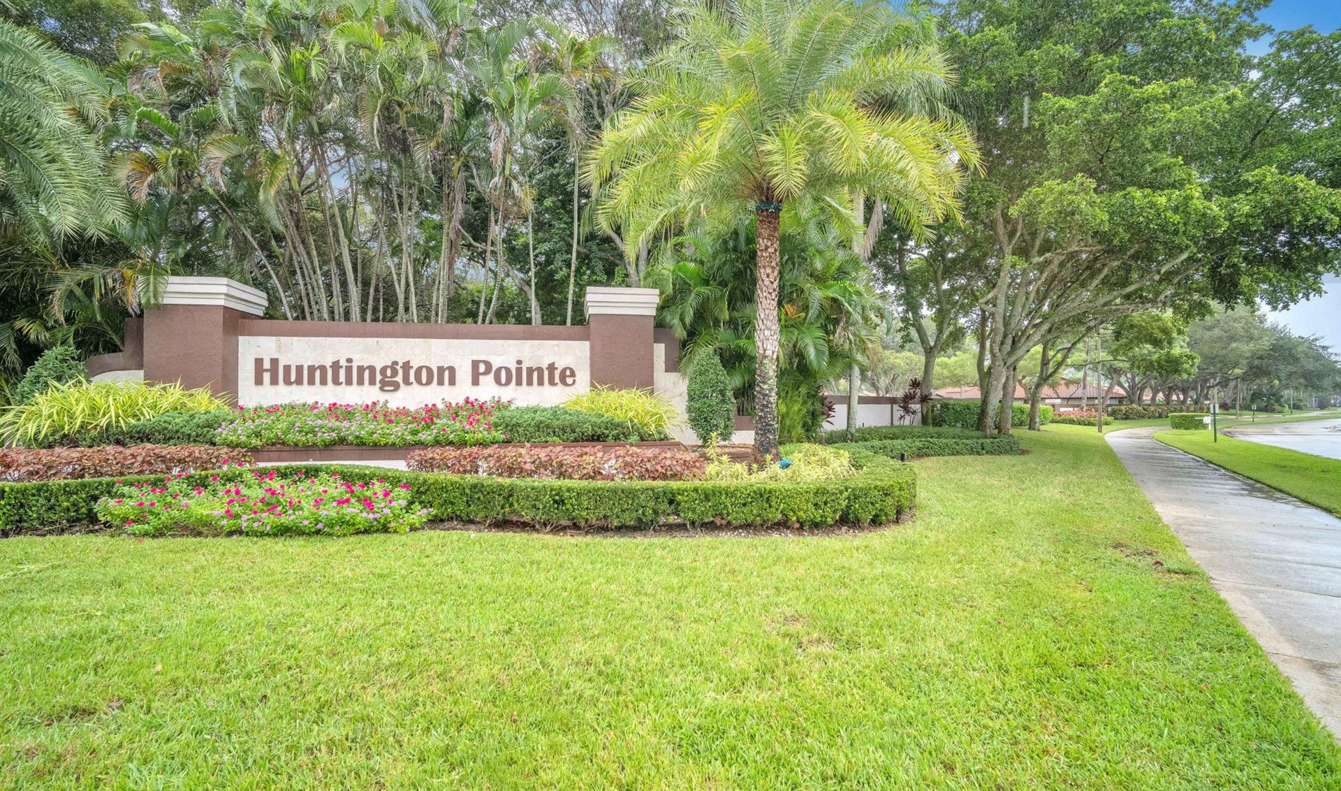 Huntington Pointe entrance sign amid tropical landscaping and flower beds.