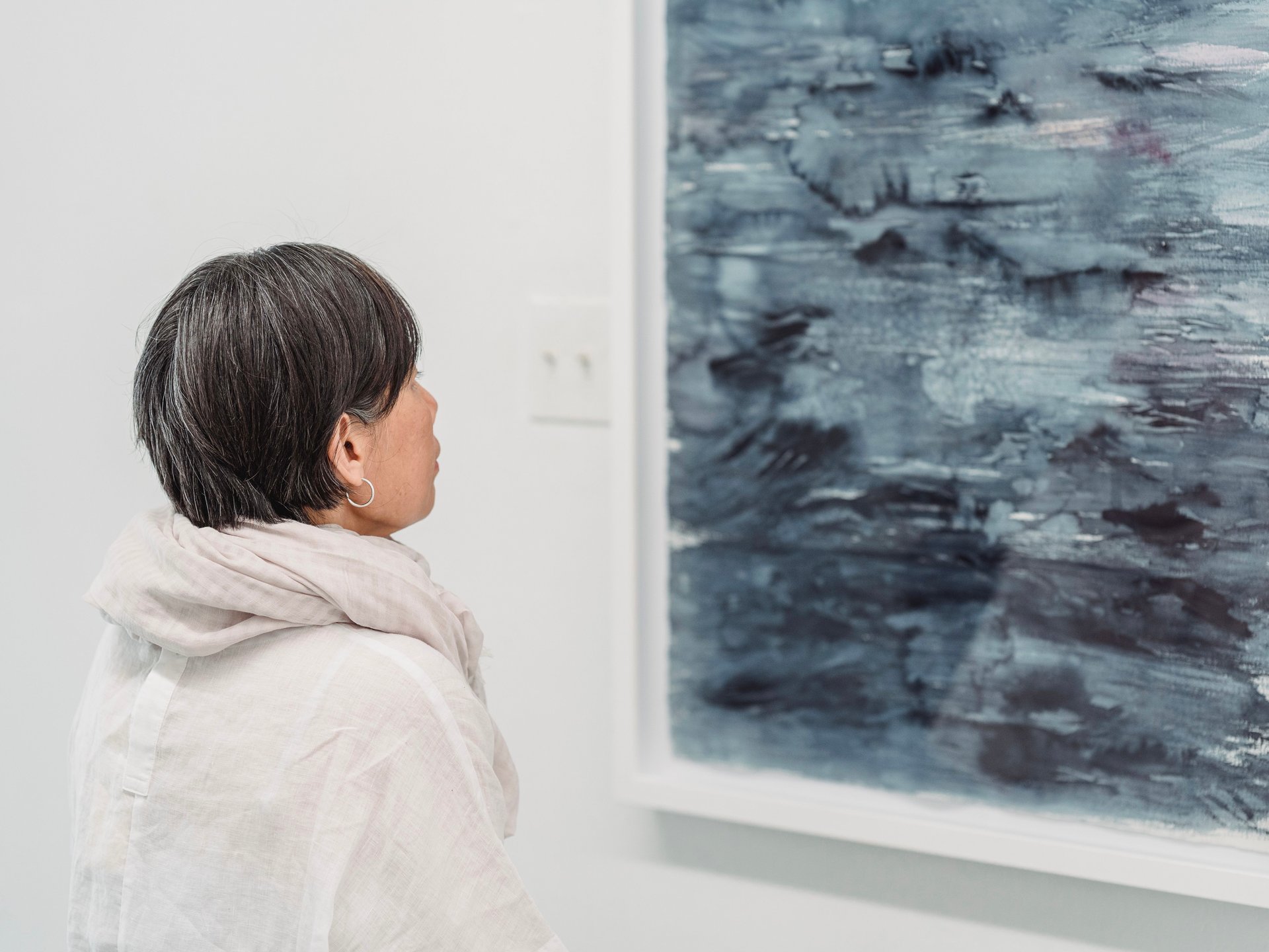 Woman in a light scarf viewing a large blue abstract painting in a gallery.