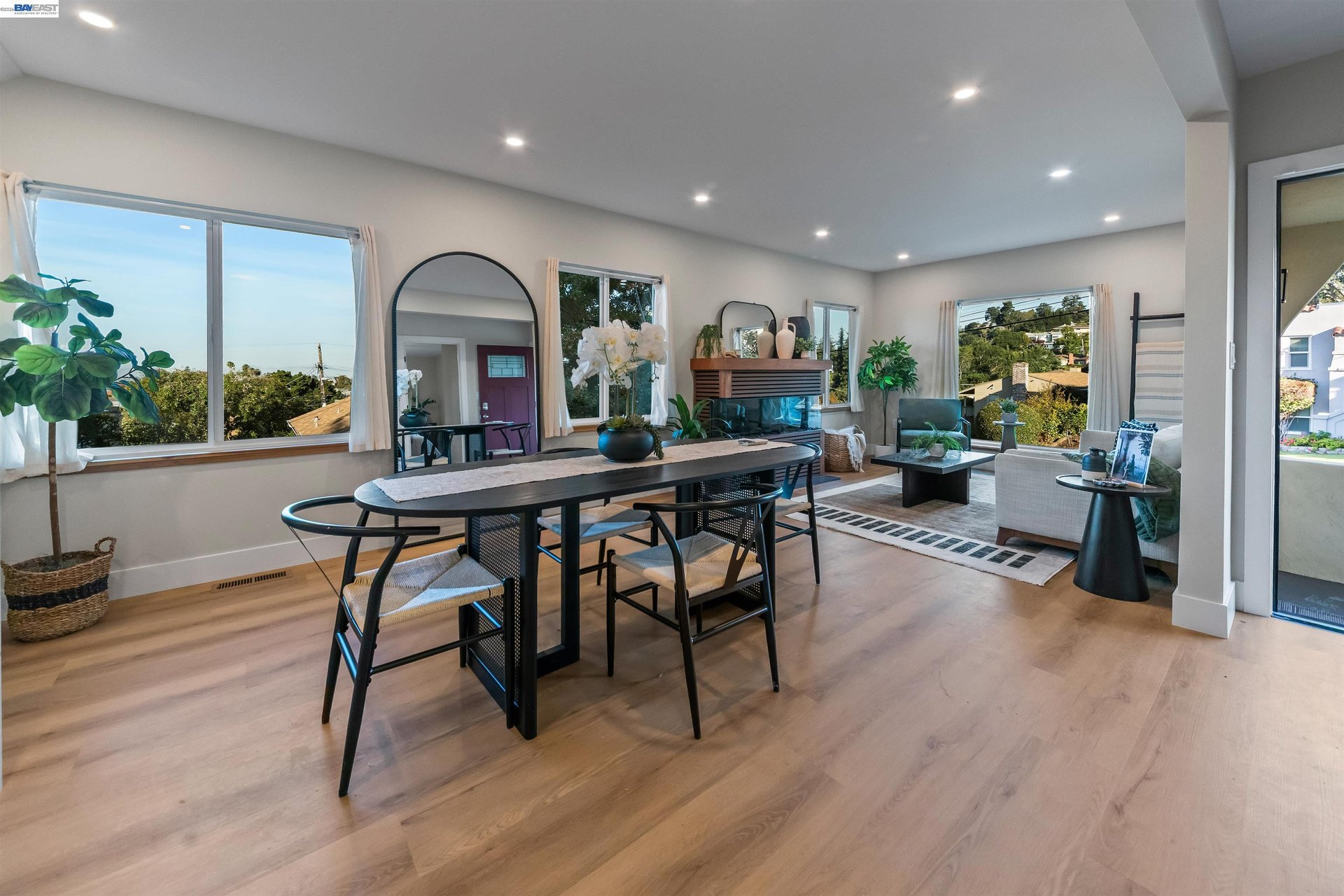 Open-plan dining and living room with a long dark table, fireplace, and large windows.