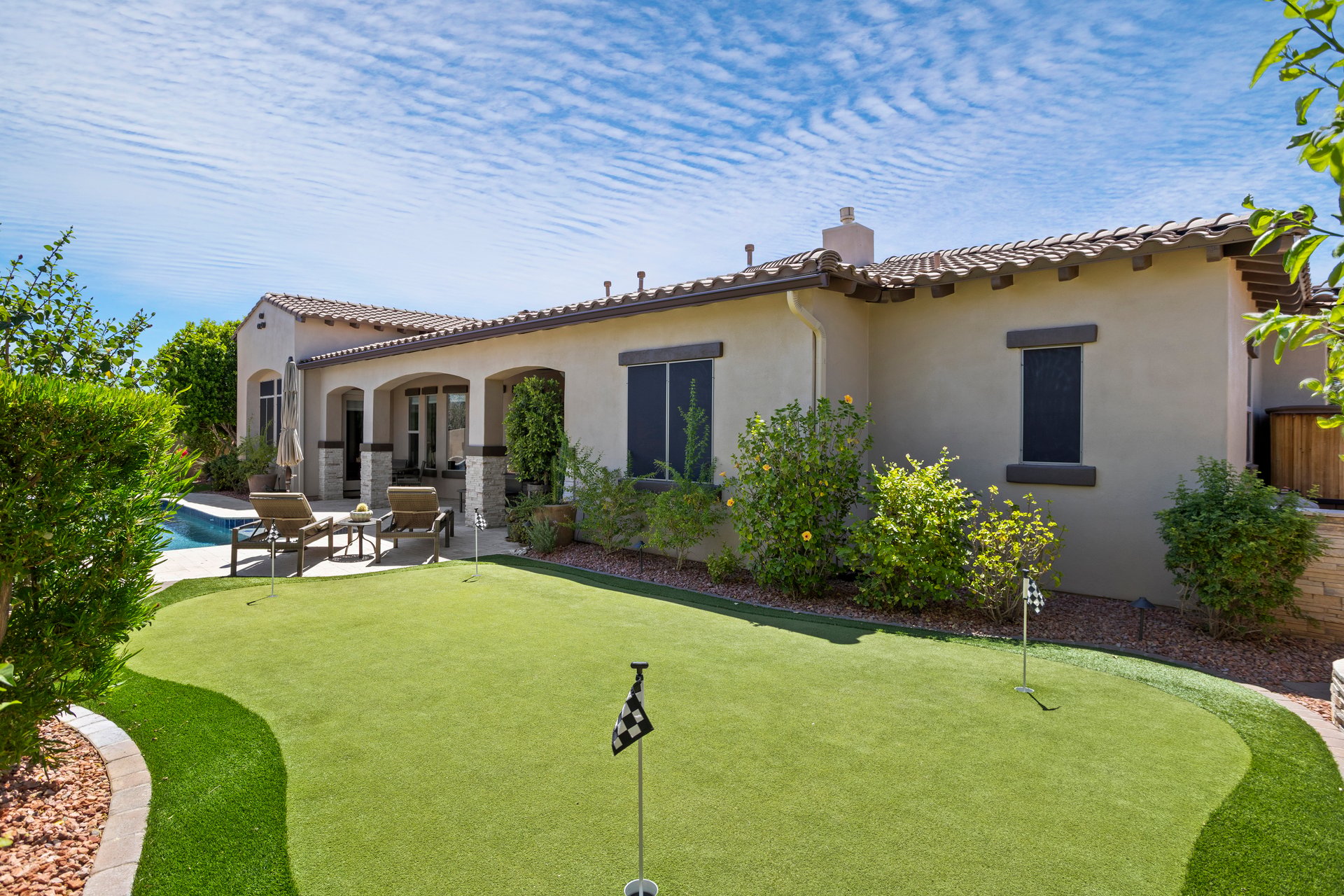 Backyard patio of a stucco house with a small pool, lounge chairs, and a putting green.