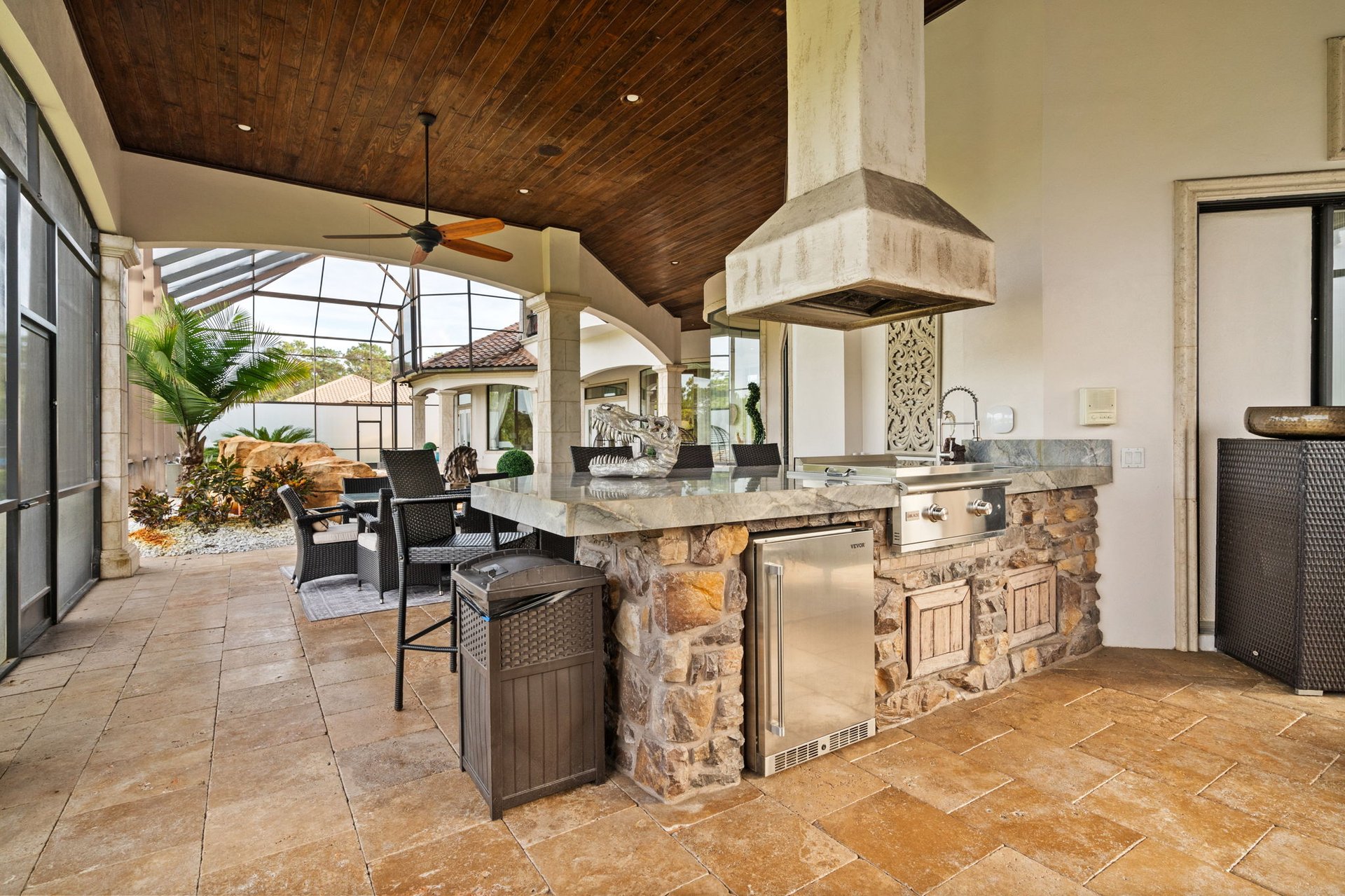 Covered outdoor kitchen with a stone island, built-in grill, and adjoining dining area.