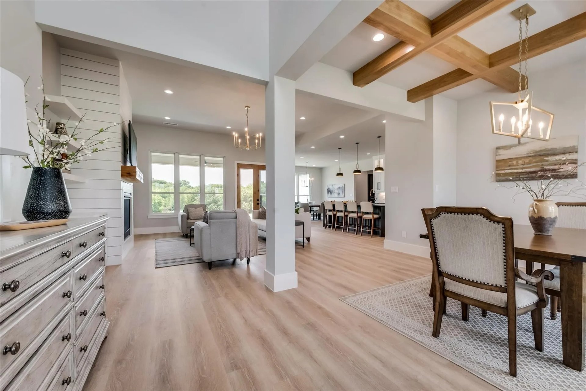 Open-concept living and dining area with exposed wood beams and light wood flooring.