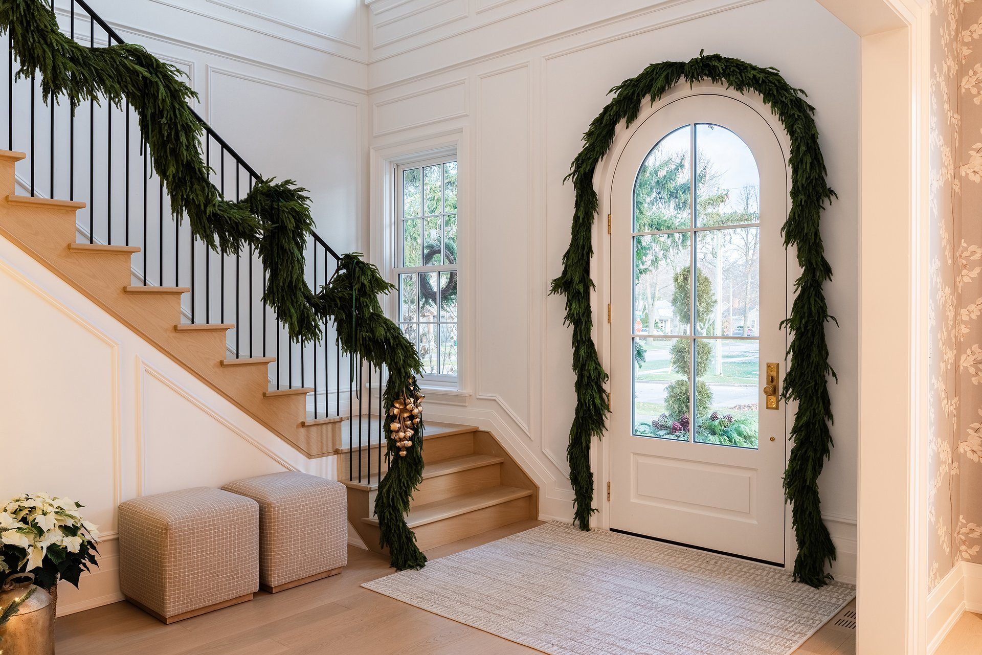 Entryway of an Oakville custom home with natural greenery garland along the staircase and arched front door.