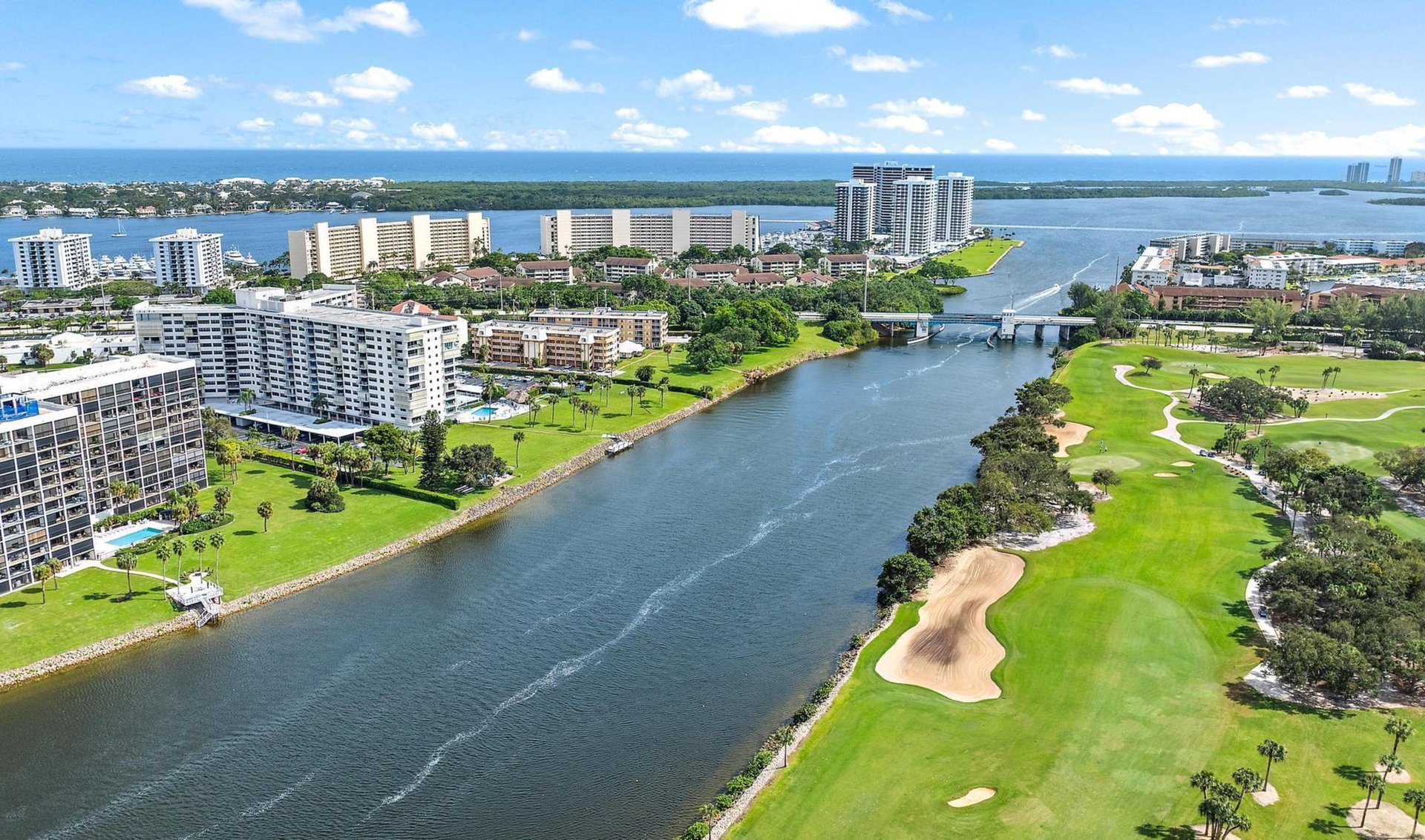 Aerial view of waterfront condos, a bridge, and a golf course beside the ocean.