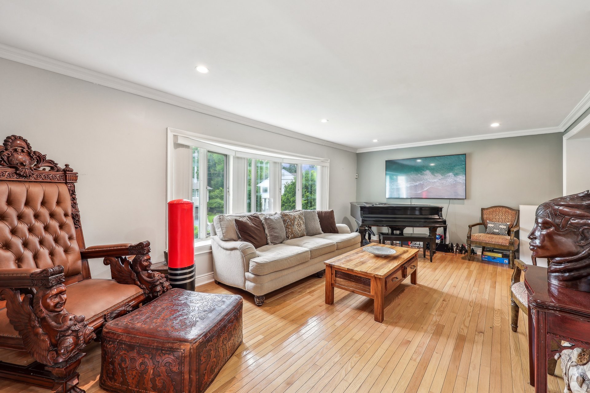 Living room with a grand piano, cream sofa, hardwood floors, and ornate carved wooden chairs.