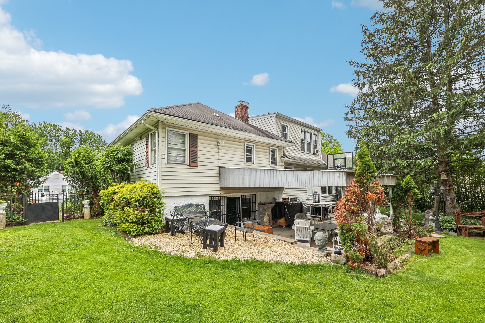 Rear of a two-story house with a covered patio, basketball hoop, and landscaped backyard.