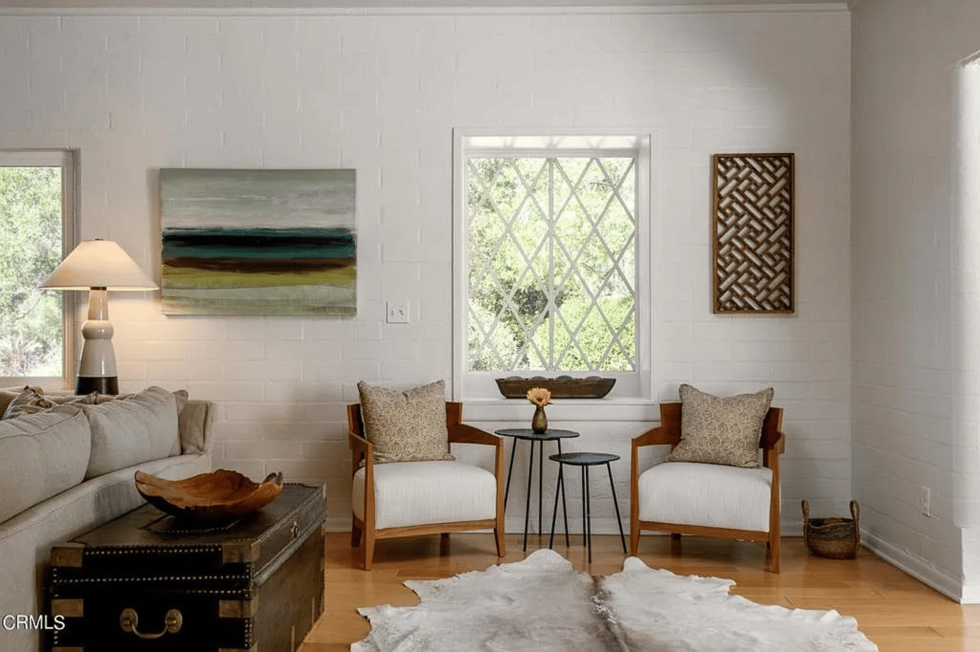Living room with white brick walls, a diamond-pane window, and two wood-framed armchairs.
