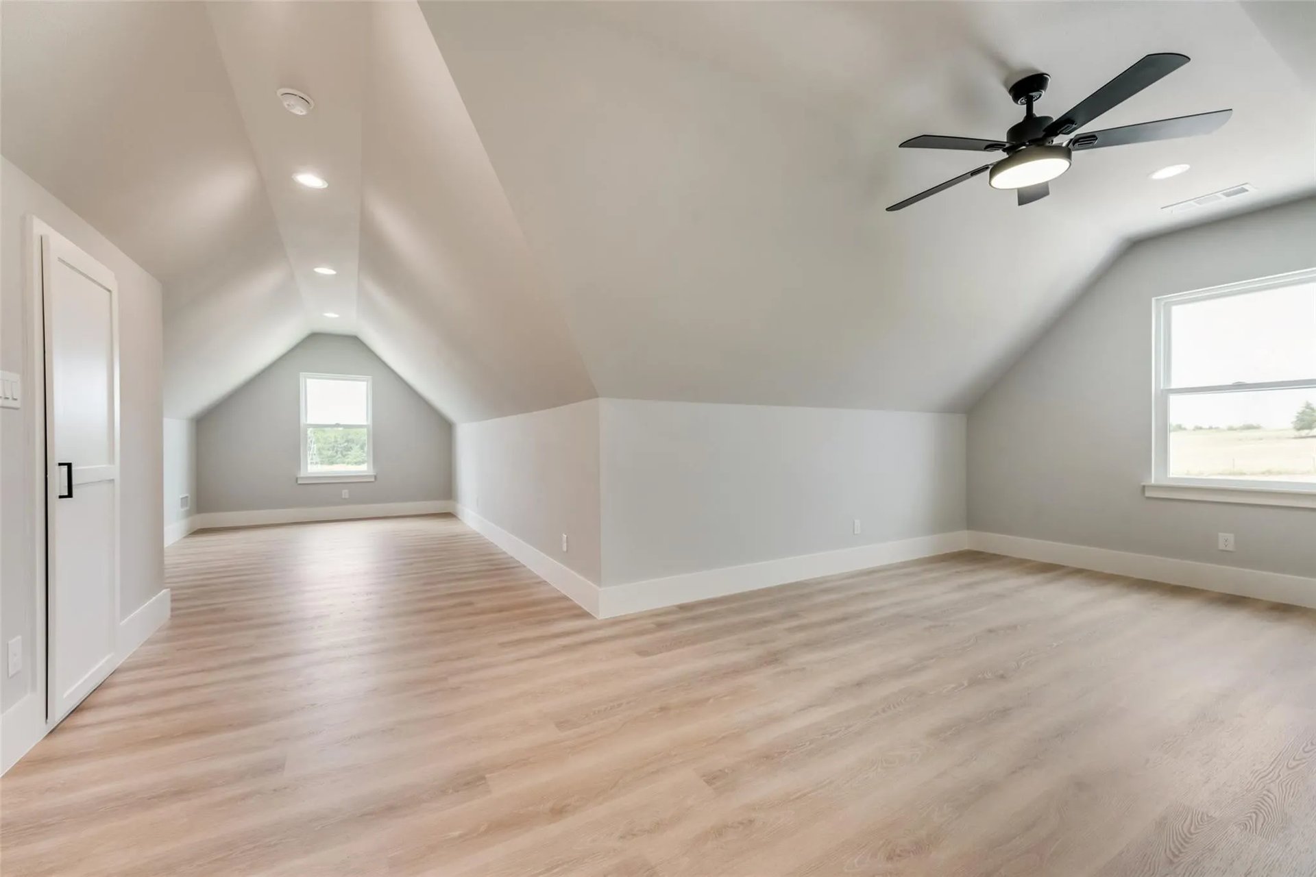 Finished attic room with sloped ceilings, light wood-look floors, and a ceiling fan.