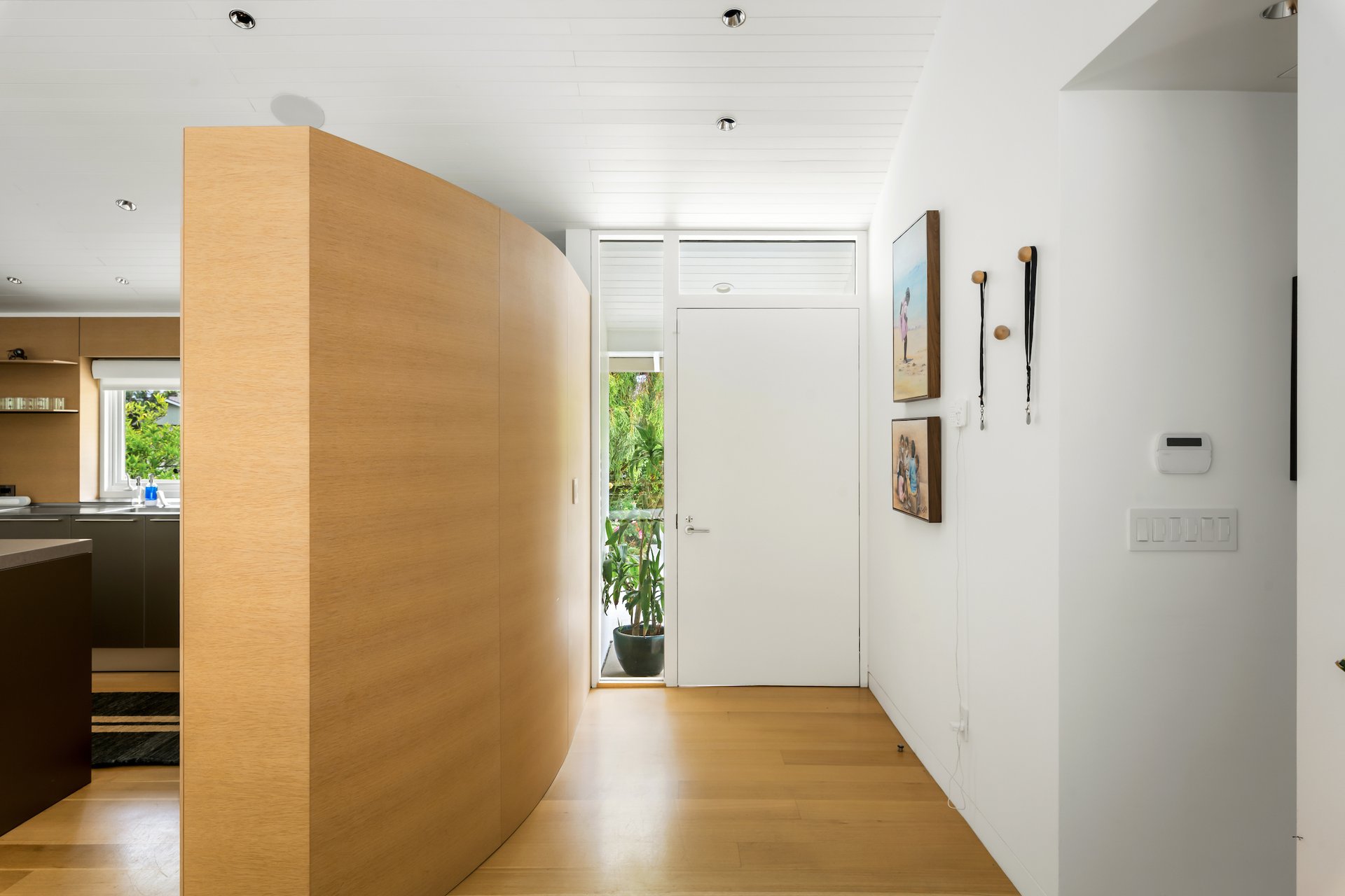 Modern entry hall with a curved wood partition, white front door, and kitchen visible to the left.