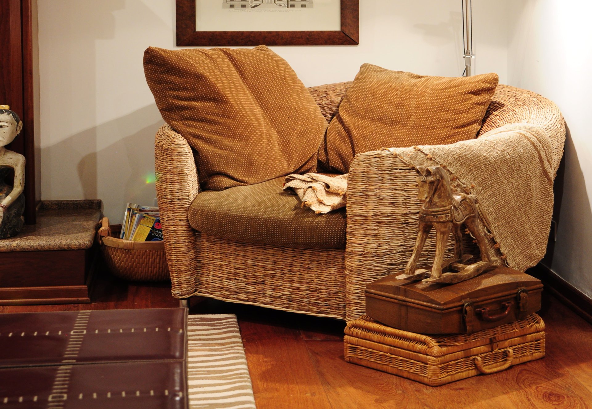 Wicker armchair with brown cushions beside a carved wooden horse on stacked vintage suitcases.