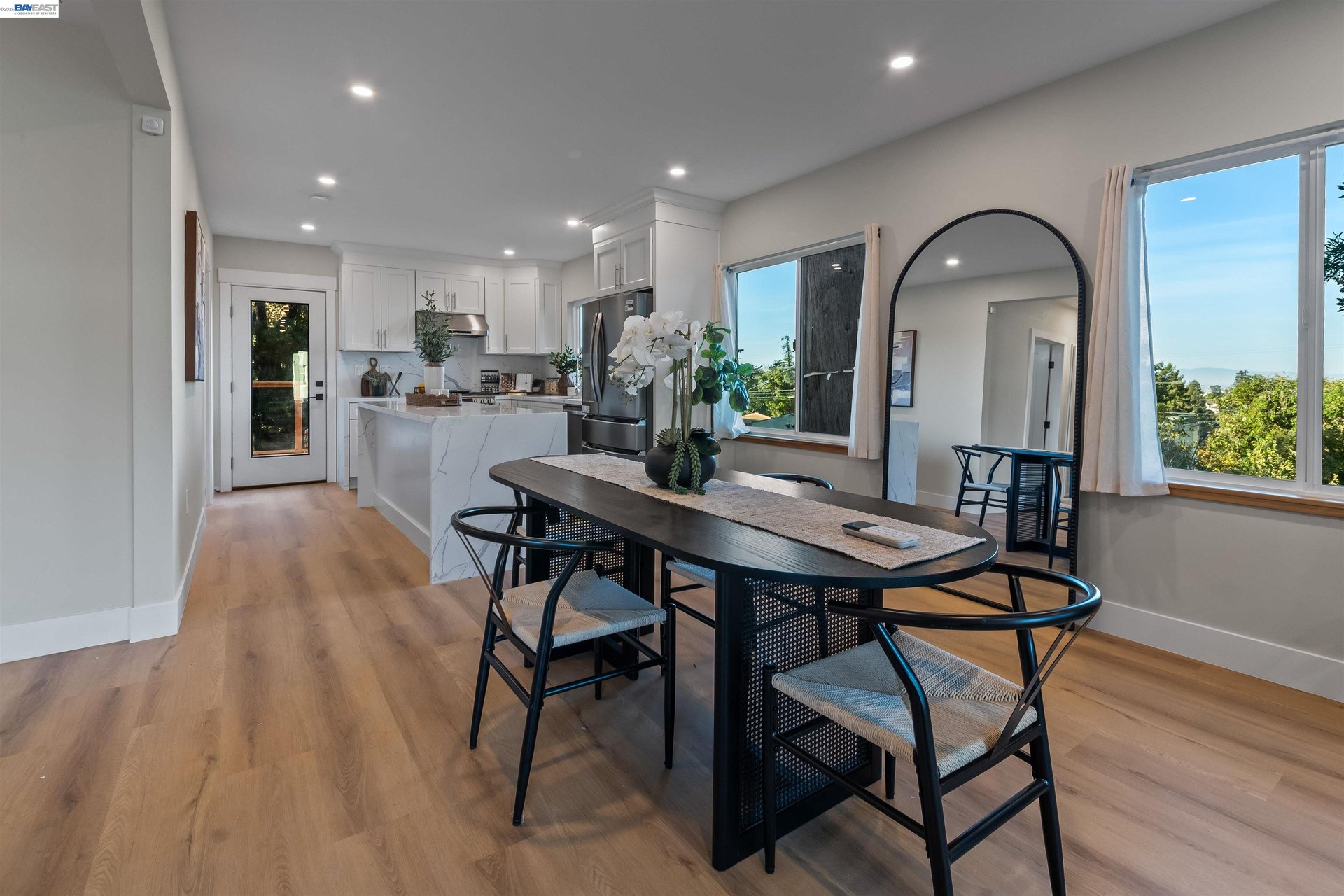 Kitchen and dining area with a marble-look island, dark table, wood floors, and large windows.