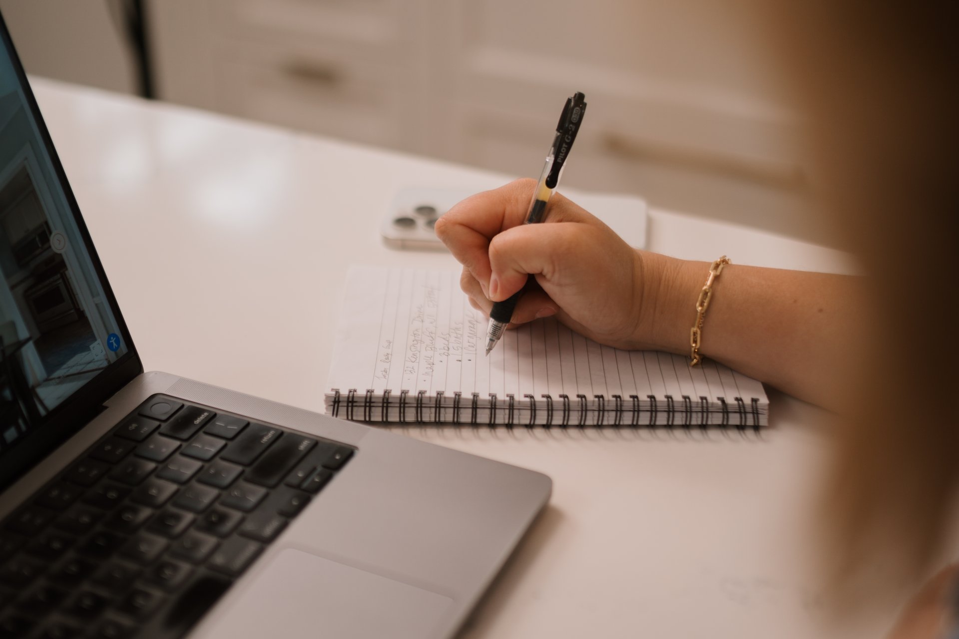Close-up over the shoulder of a buyer writing notes on a spiral pad next to a laptop, representing the careful preparation and strategy needed to write a winning real estate offer in Sun Prairie.