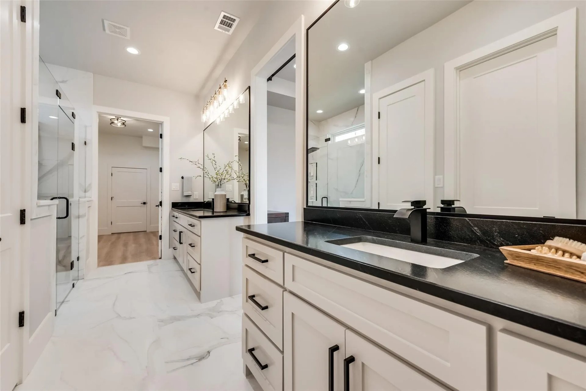 Bathroom with white cabinetry, black counters, a large mirror, and glass shower.