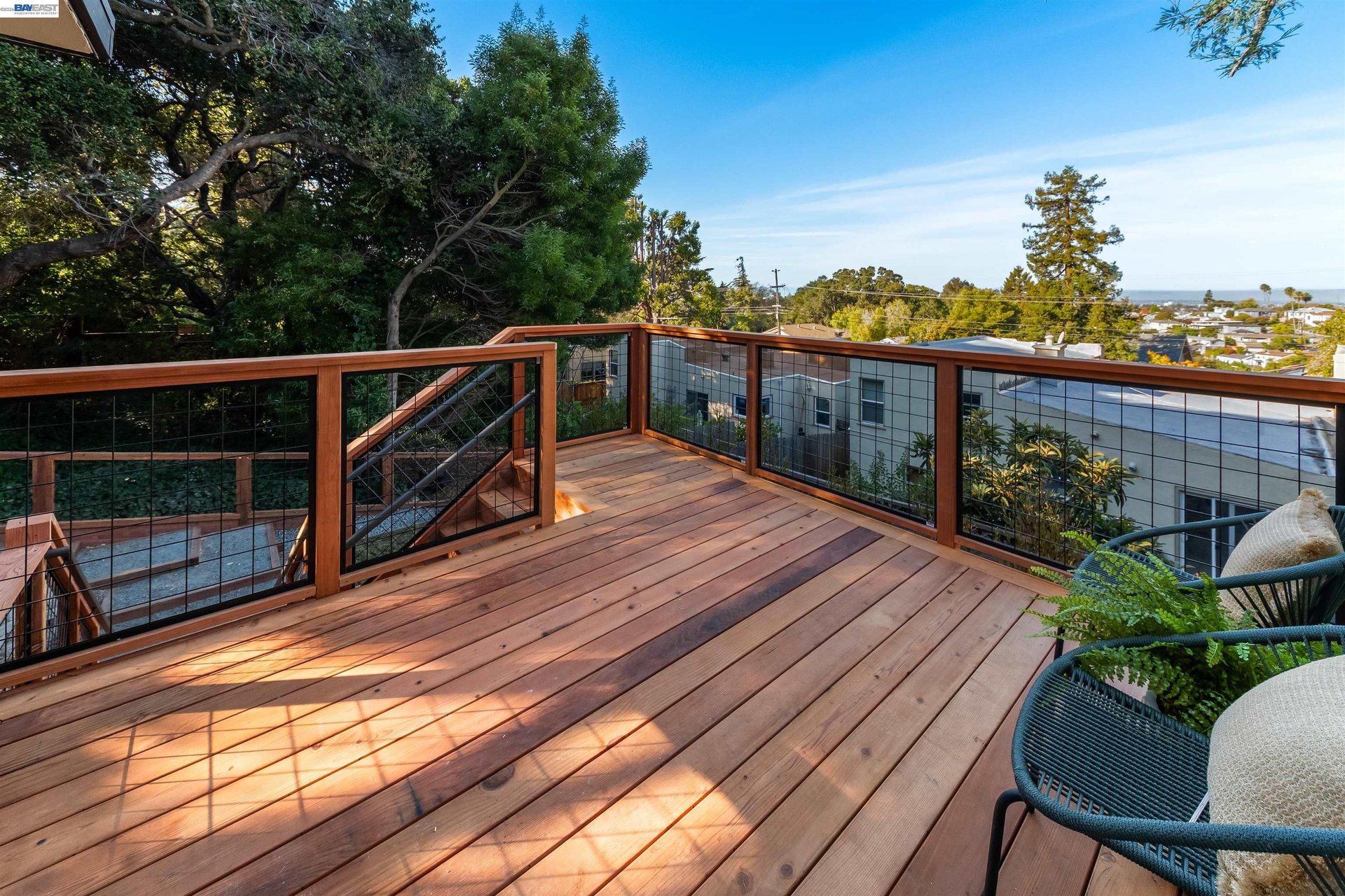 Wooden deck with cable railings and seating overlooking treetops and neighborhood rooftops.