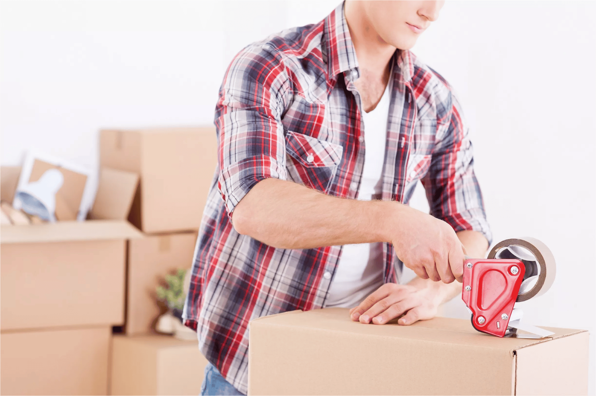 A man seals a cardboard moving box with a red tape dispenser.