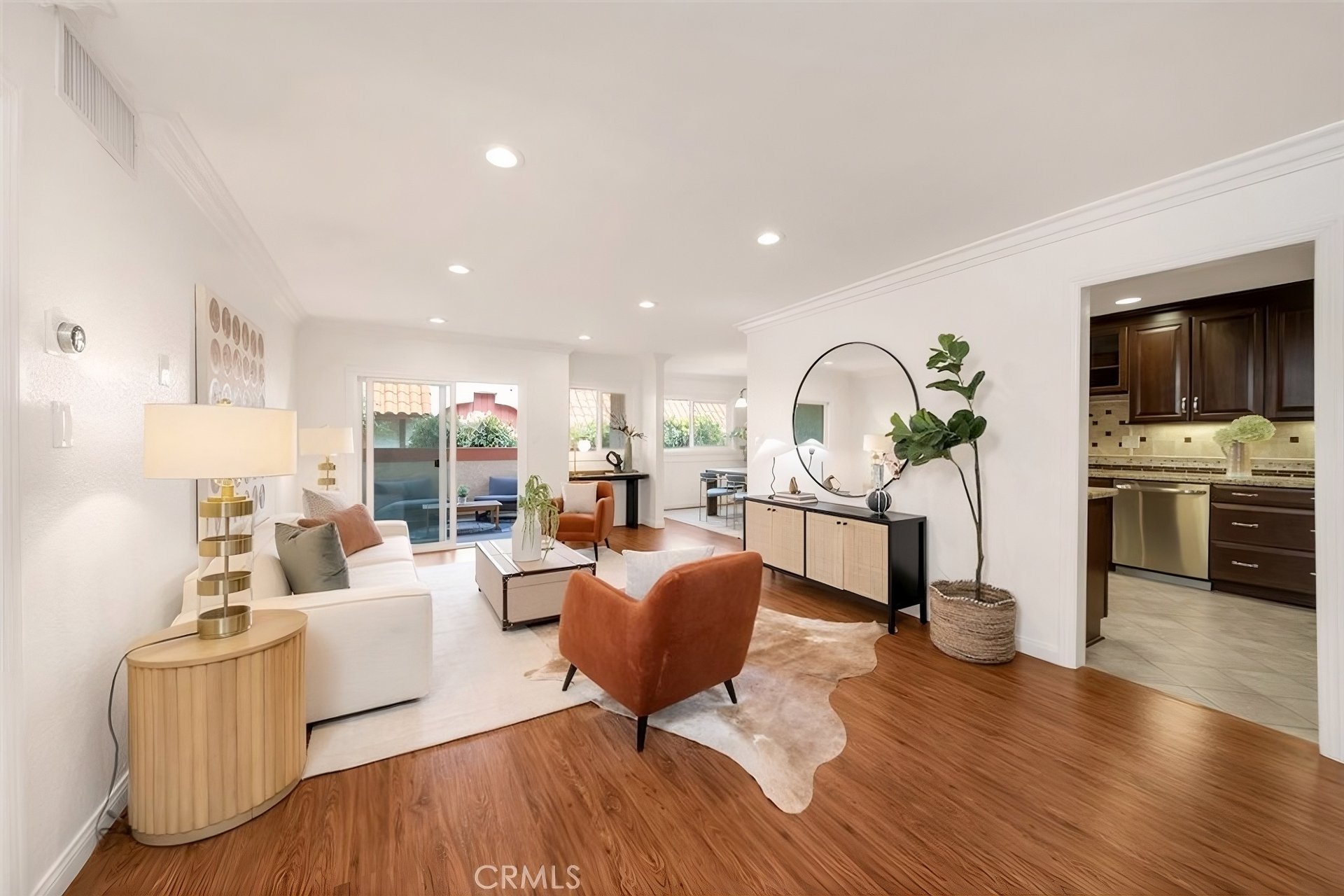Staged condo living room with wood floors, rust-colored armchairs, and sliding doors to a patio.