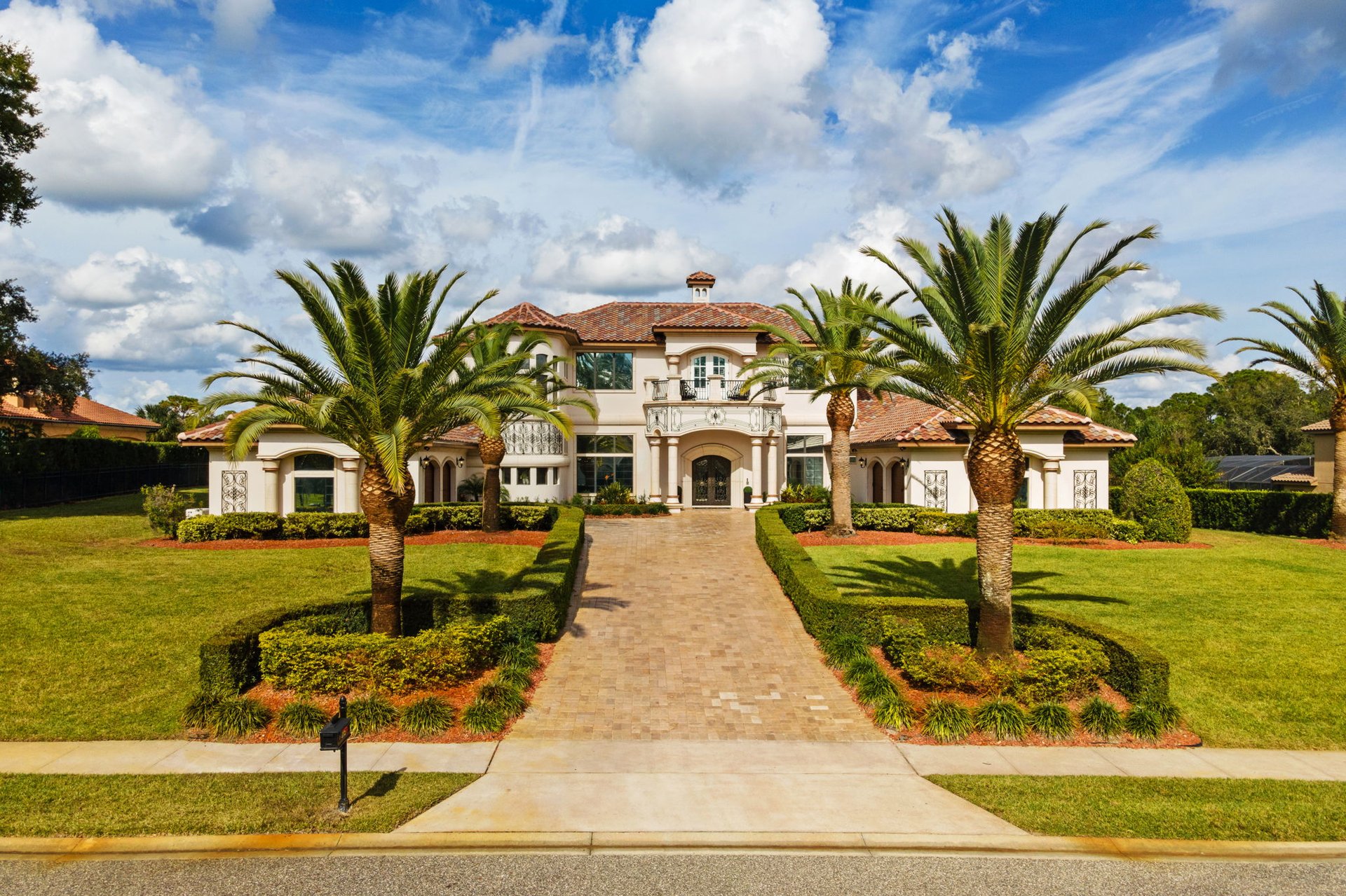 Mediterranean-style home with a terracotta roof, palm trees, and a landscaped driveway.