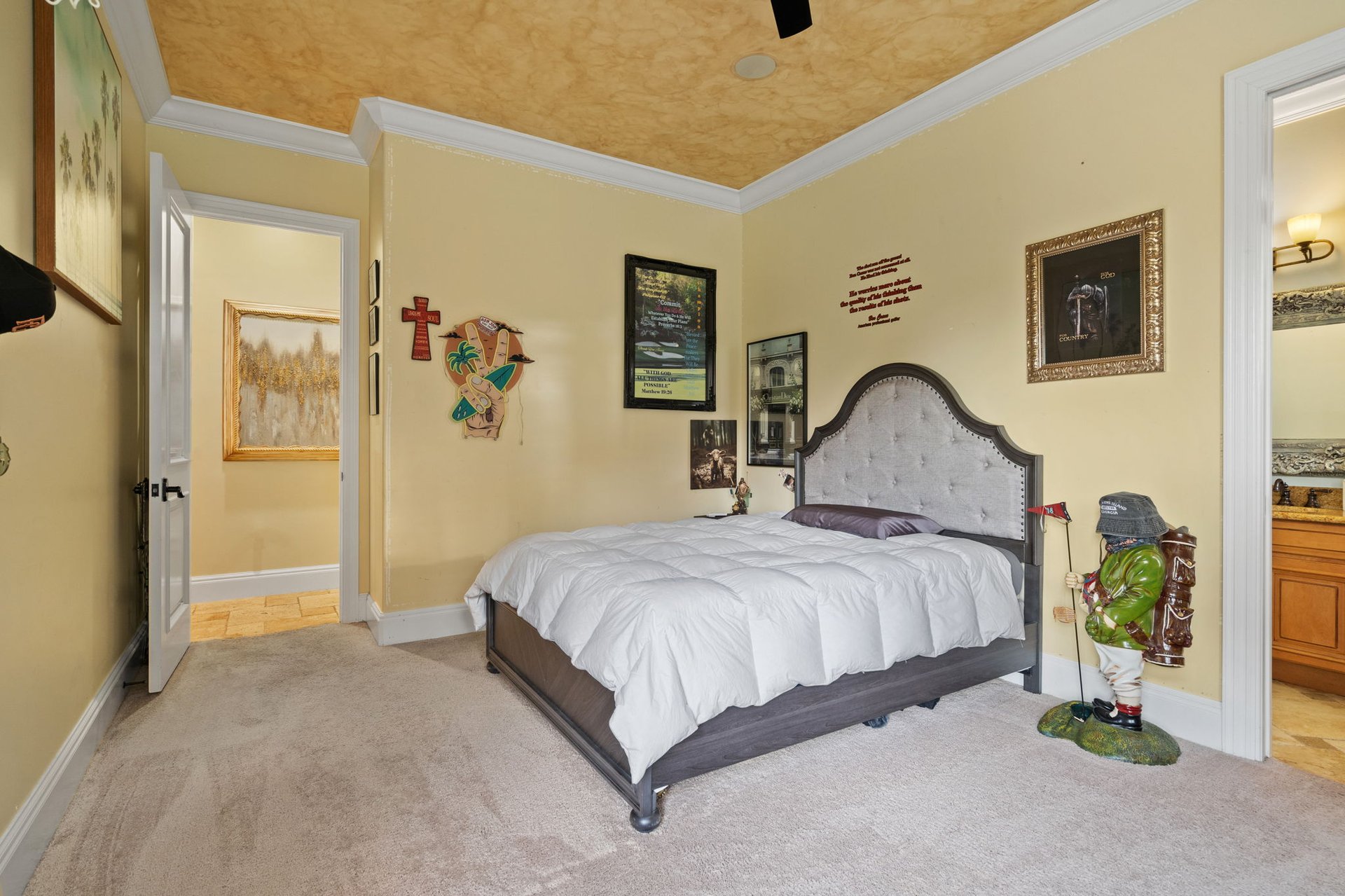 Furnished bedroom with a large bed, tufted gray headboard, textured gold ceiling, and decorative figurines.