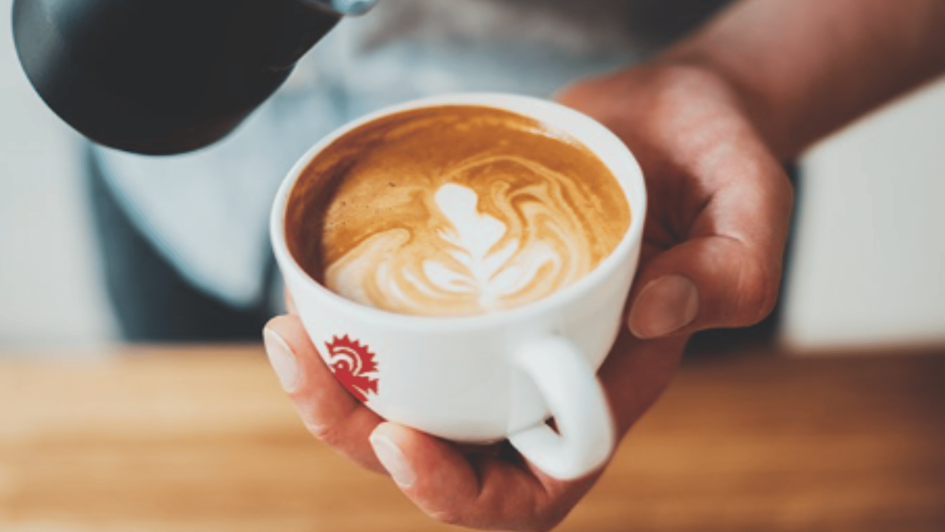 Hands holding white coffee cup with heart latte art design - Miami's expert barista work featured by The Edit Real Estate