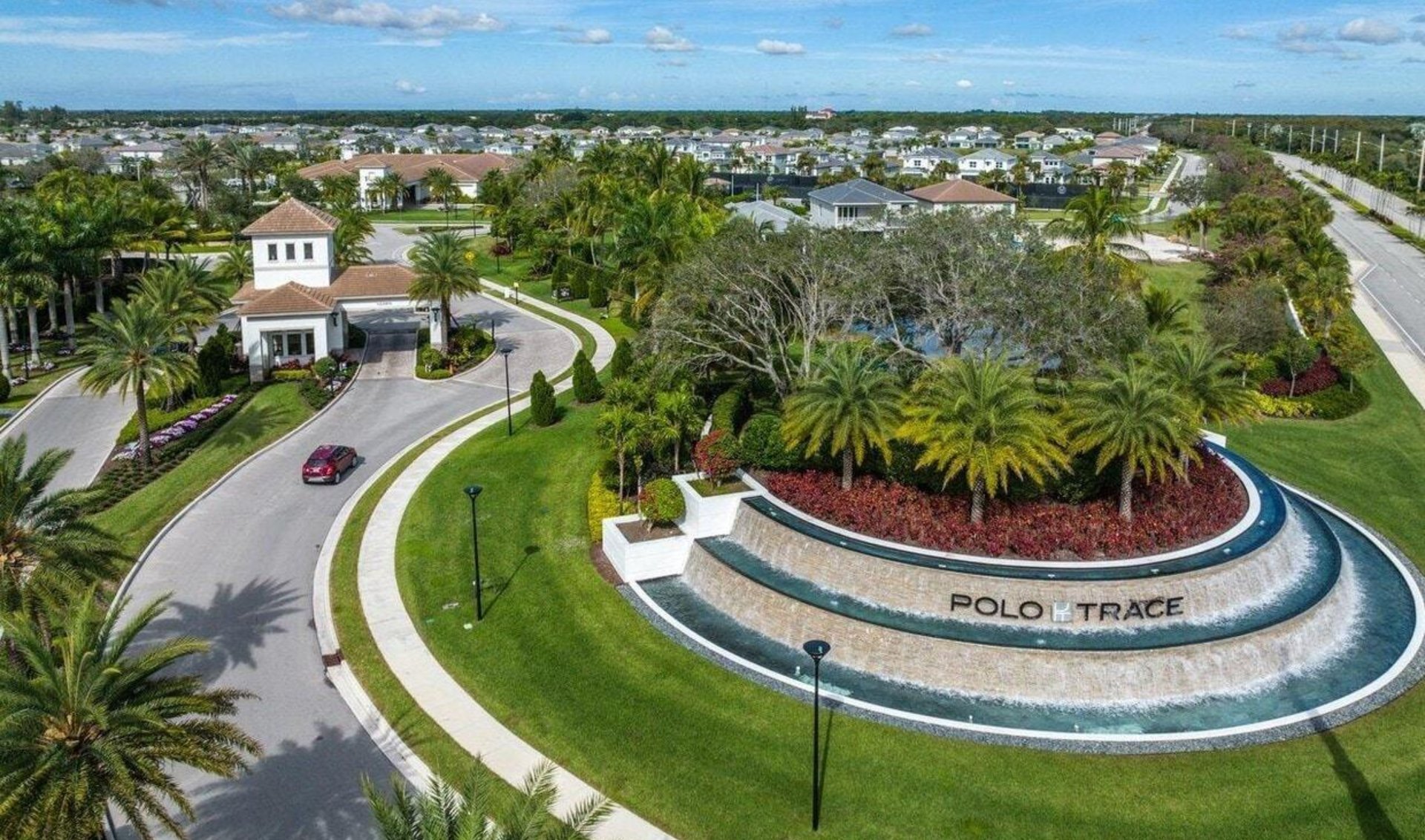 Polo Trace entrance with a tiered fountain, guardhouse, palm trees, and surrounding homes.