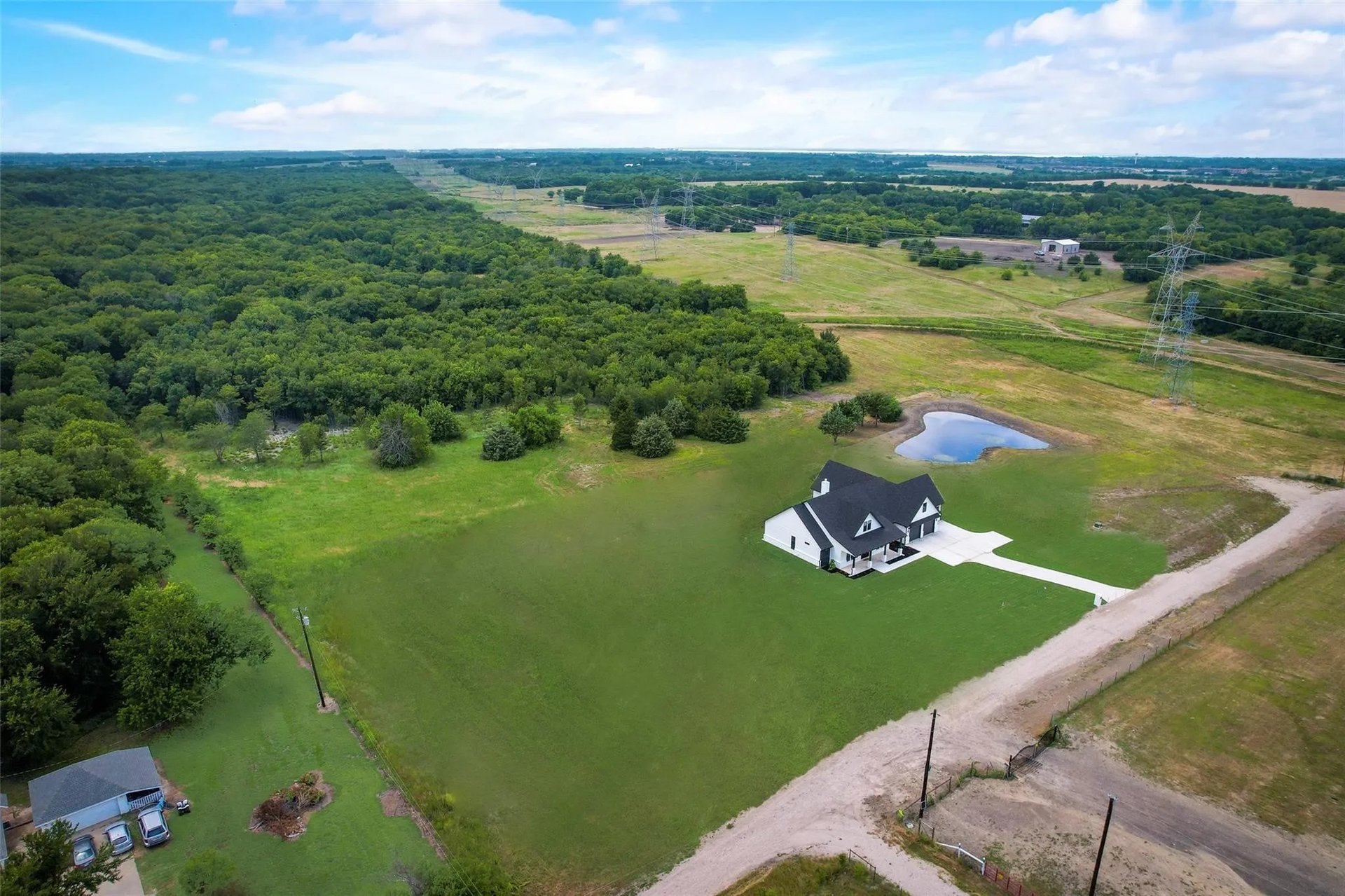 Aerial view of a white house on a broad lawn beside woods and a small pond.