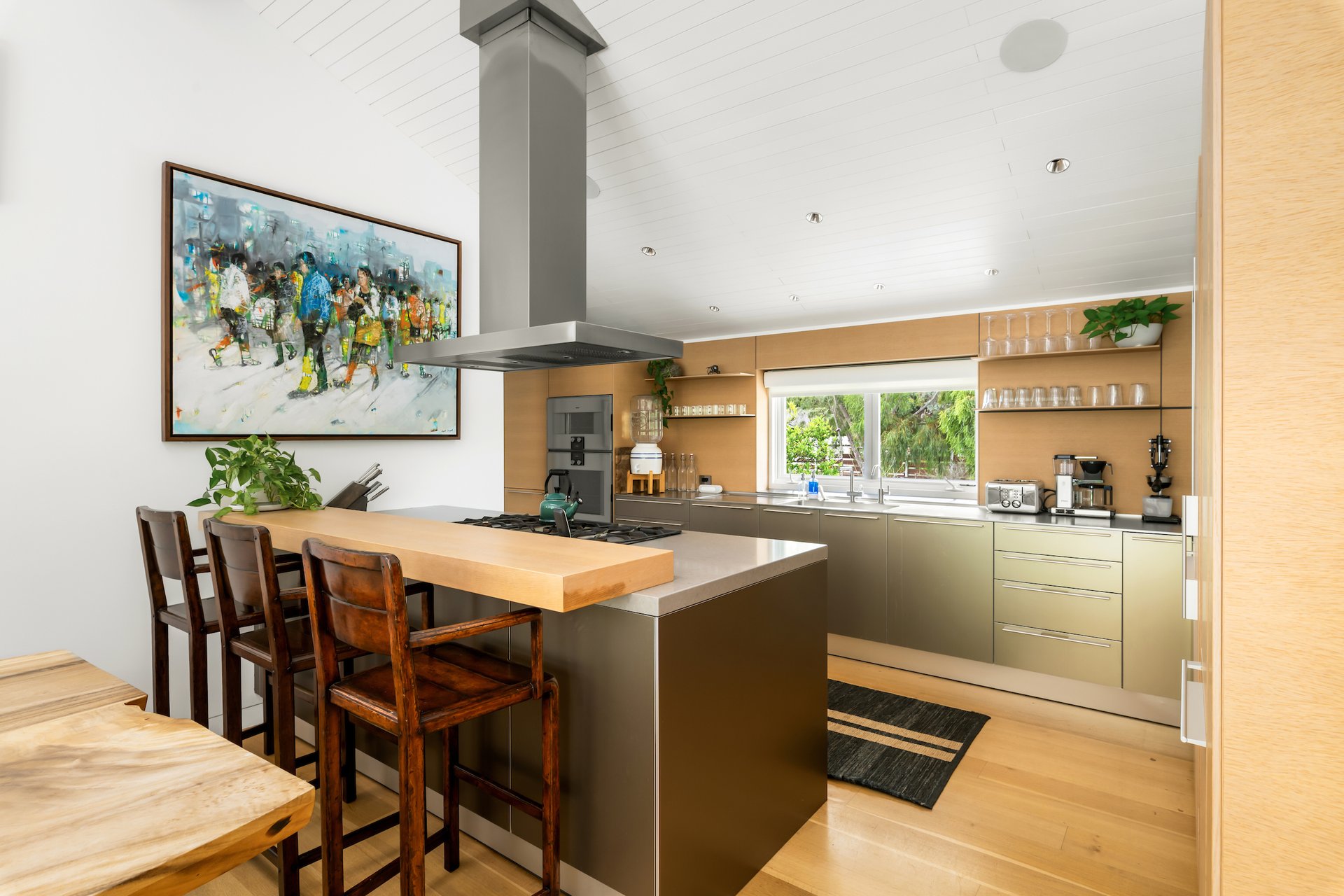 Modern kitchen with a wood breakfast bar, dark island, and wide window overlooking greenery.