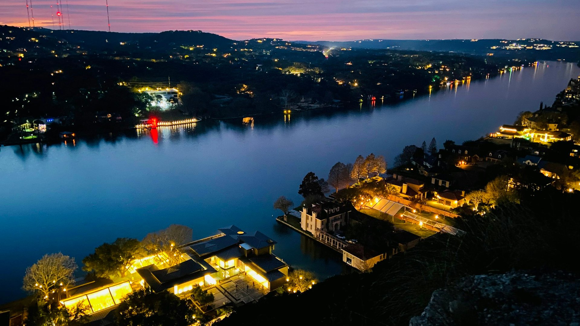 Lake Austin at dusk, waterfront houses lit along both banks.