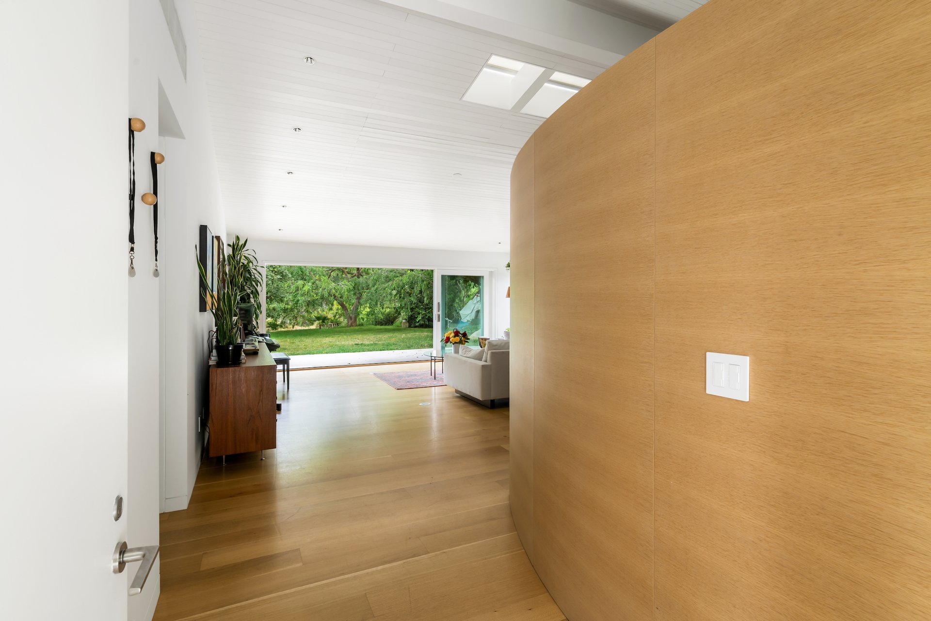 Living room with a curved wood-paneled wall and wide glass doors opening to a garden.