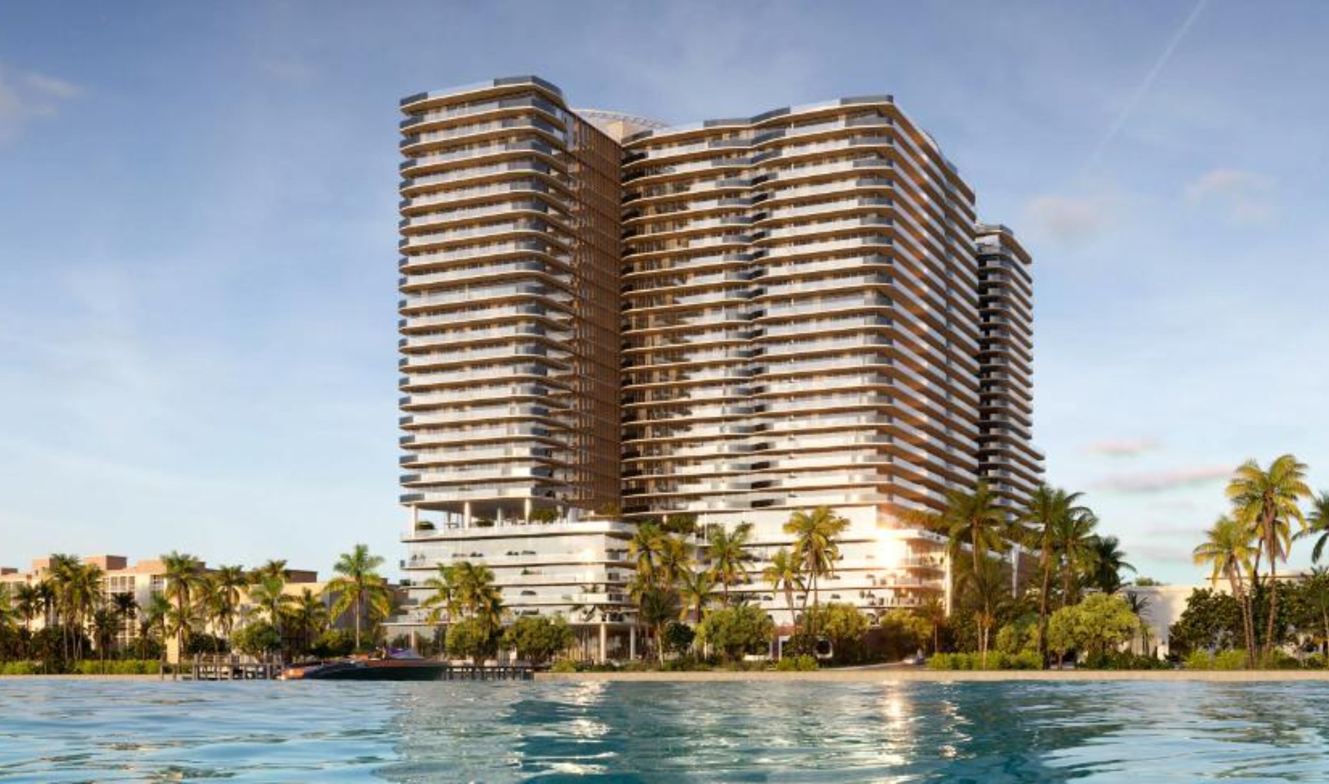 Modern waterfront condominium tower with curved balconies, palm trees, and landscaped grounds.