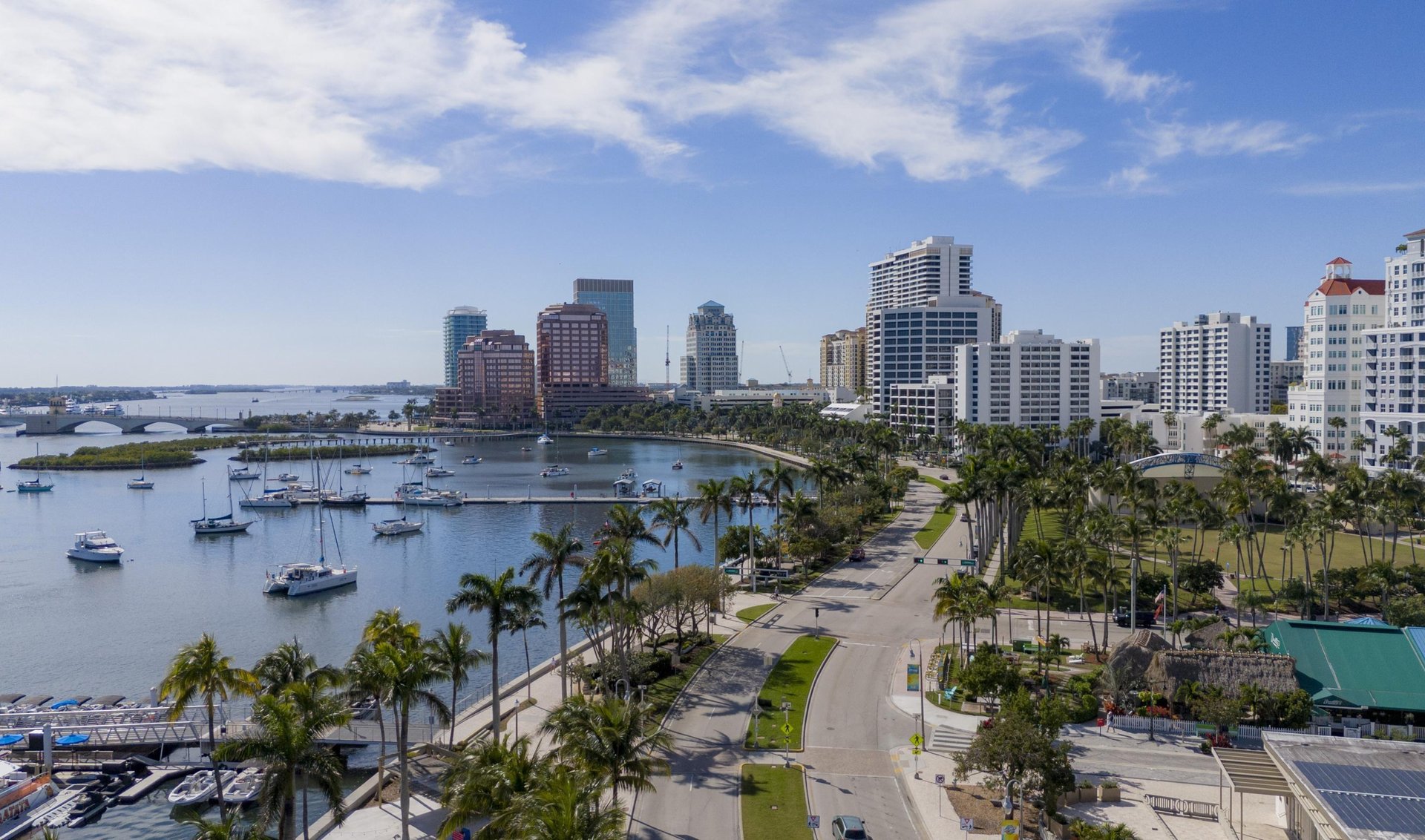 Downtown West Palm Beach waterfront with marina sailboats, high-rises, and palm-lined streets.