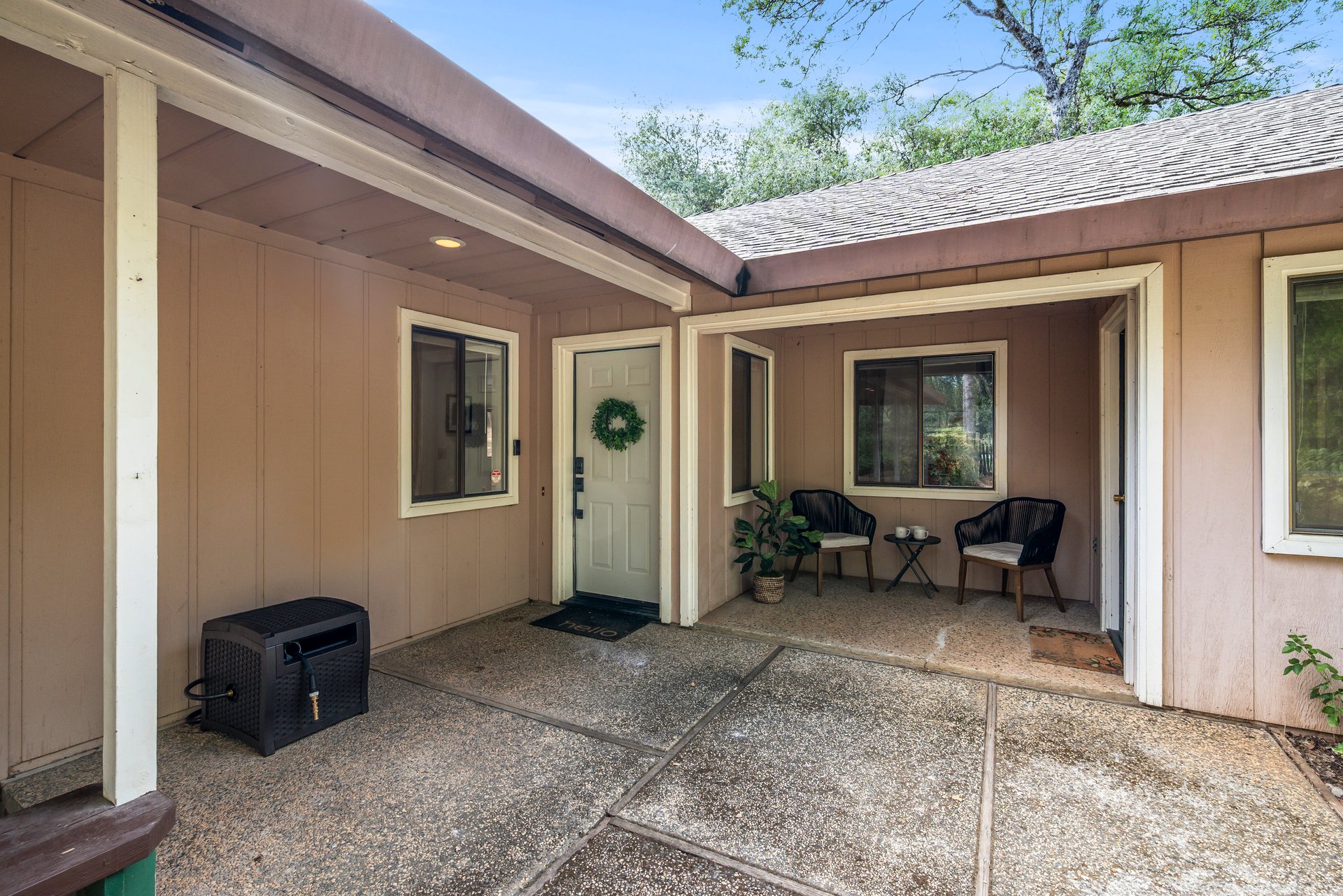 Covered entry patio with two black chairs, a small table, and a white front door.