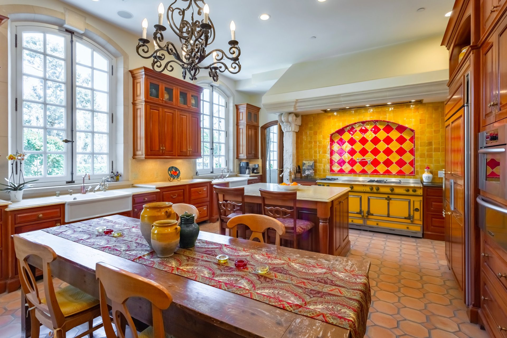 Spacious kitchen with arched windows, warm wood cabinetry, and a yellow range against a colorful tile backsplash.