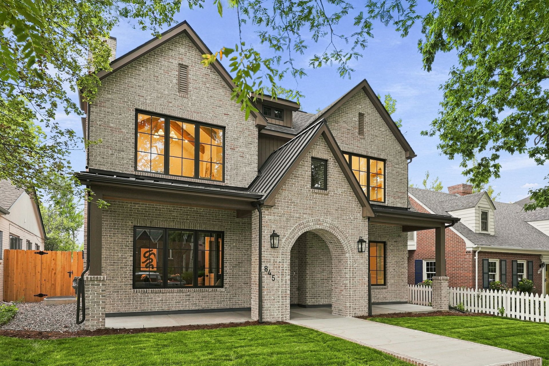 Two-story brick home with steep gables, black-framed windows, and an arched covered entry.