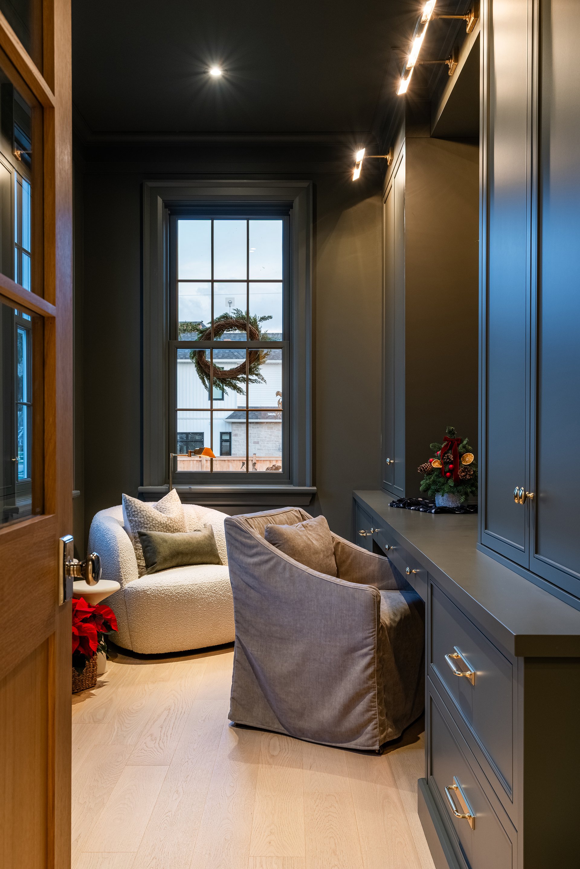 Home office in an Oakville custom home with built-in cabinetry, soft seating, and seasonal wreath on the window.