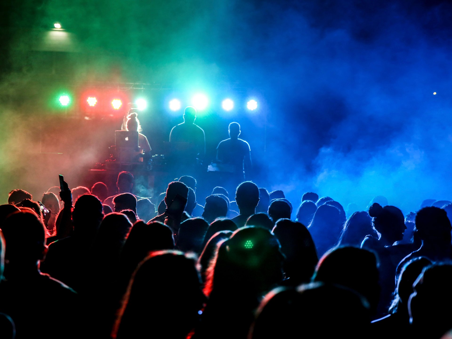 Concert crowd watching performers under vivid blue, red, and green stage lights.