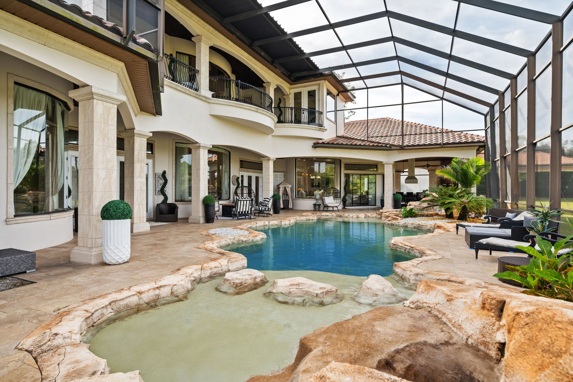 Backyard pool and raised stone spa beneath a screened enclosure beside a two-story home.