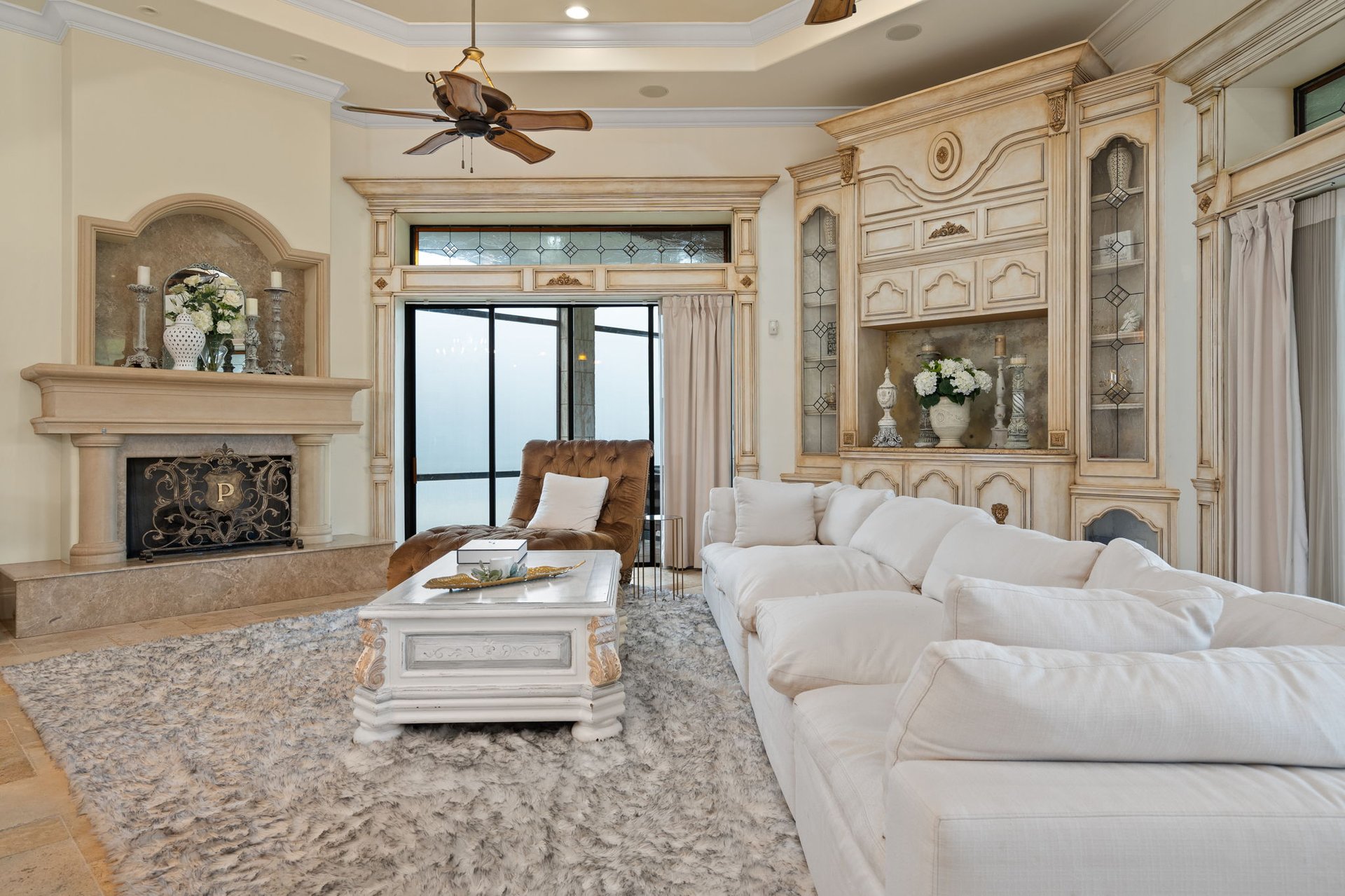 Living room with a white sectional, ornate built-ins, stone fireplace, and sliding glass doors.