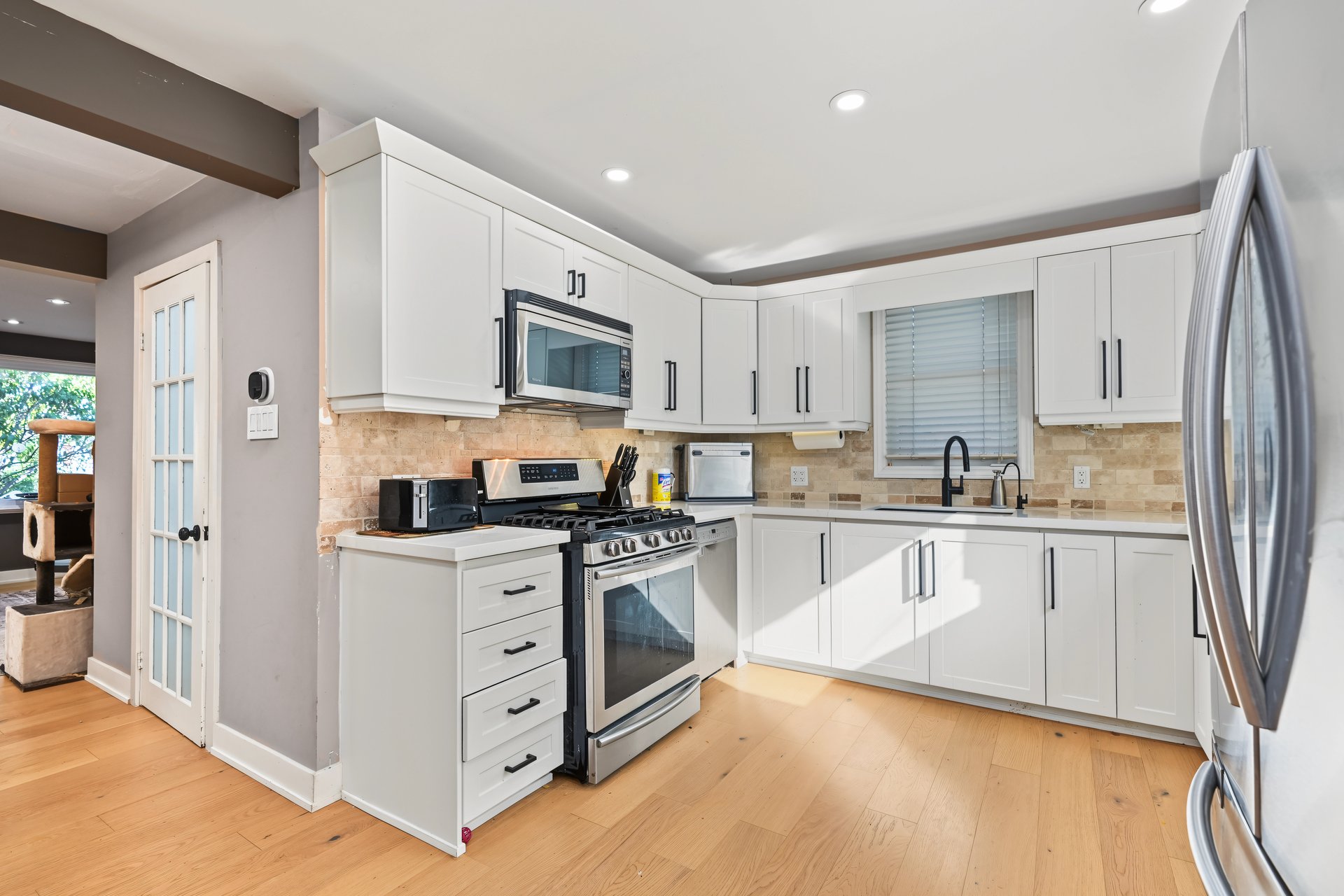 Kitchen with white cabinets, stainless steel appliances, and a gas range beside a beige tile backsplash.