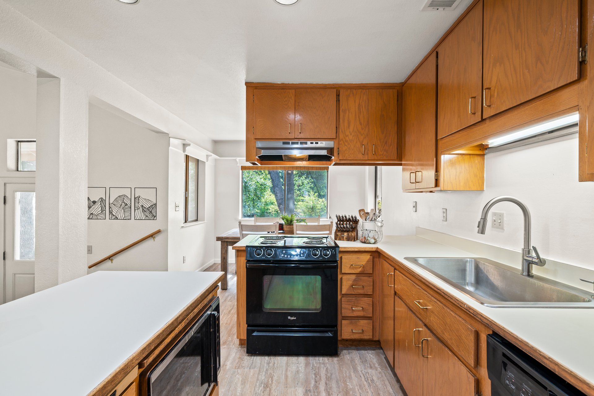 Kitchen with warm wood cabinets, white countertops, a black range, and a stainless-steel sink.