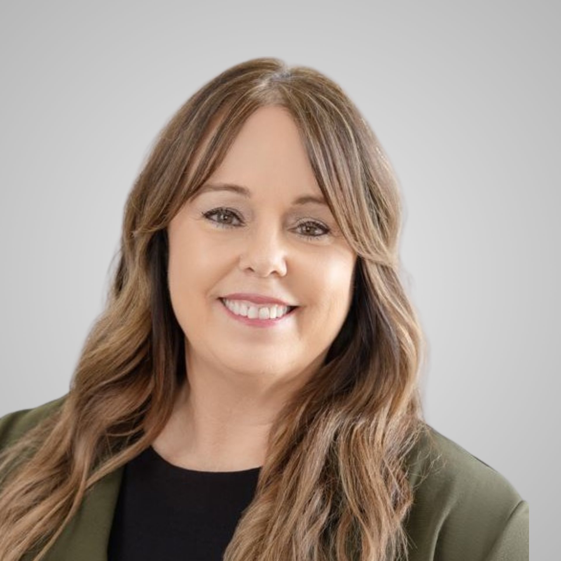 Megan Carr smiling in an olive blazer, with long highlighted brown hair.