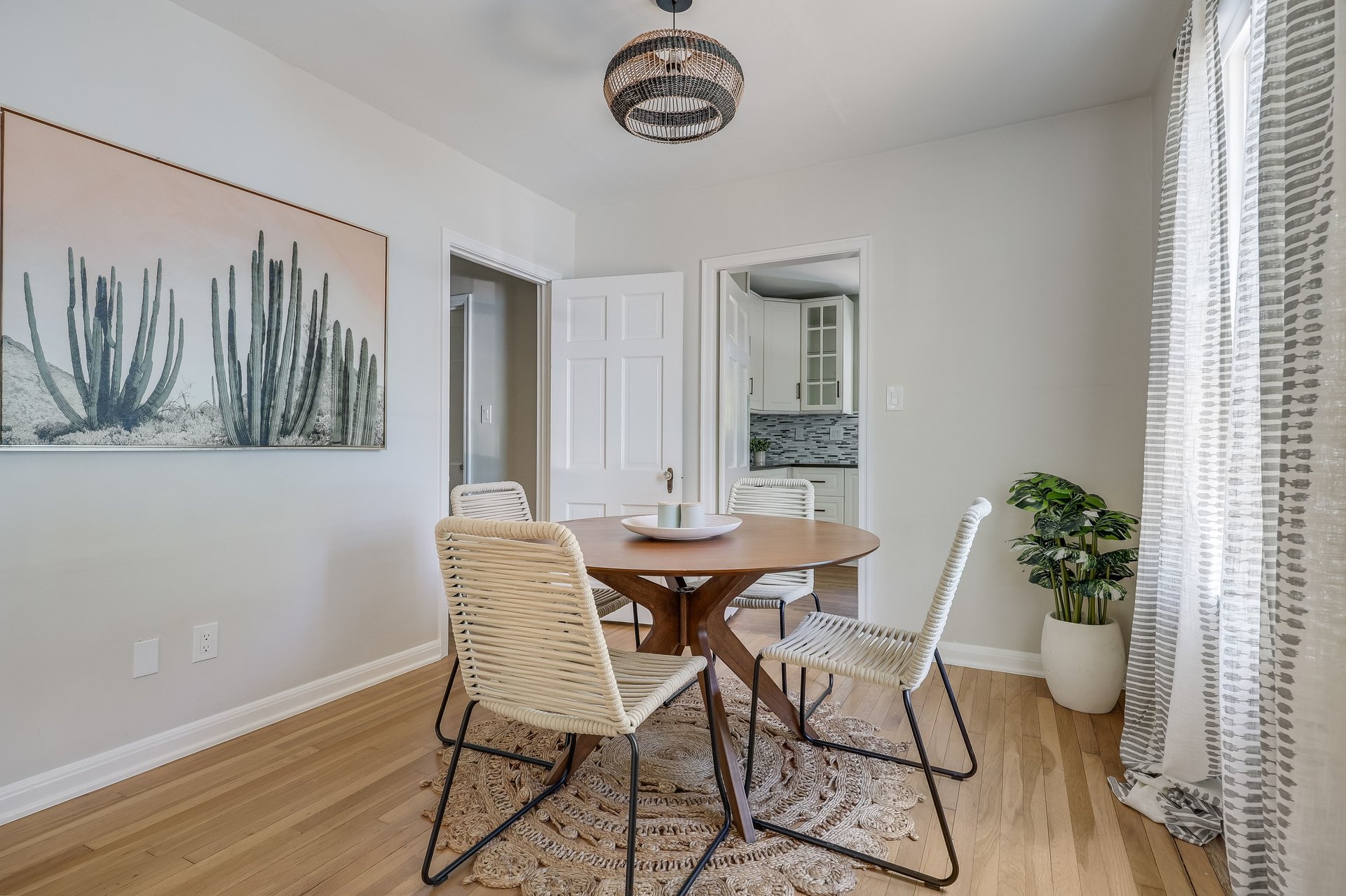 Furnished dining room with a round table, woven chairs, cactus artwork, and a doorway to the kitchen.