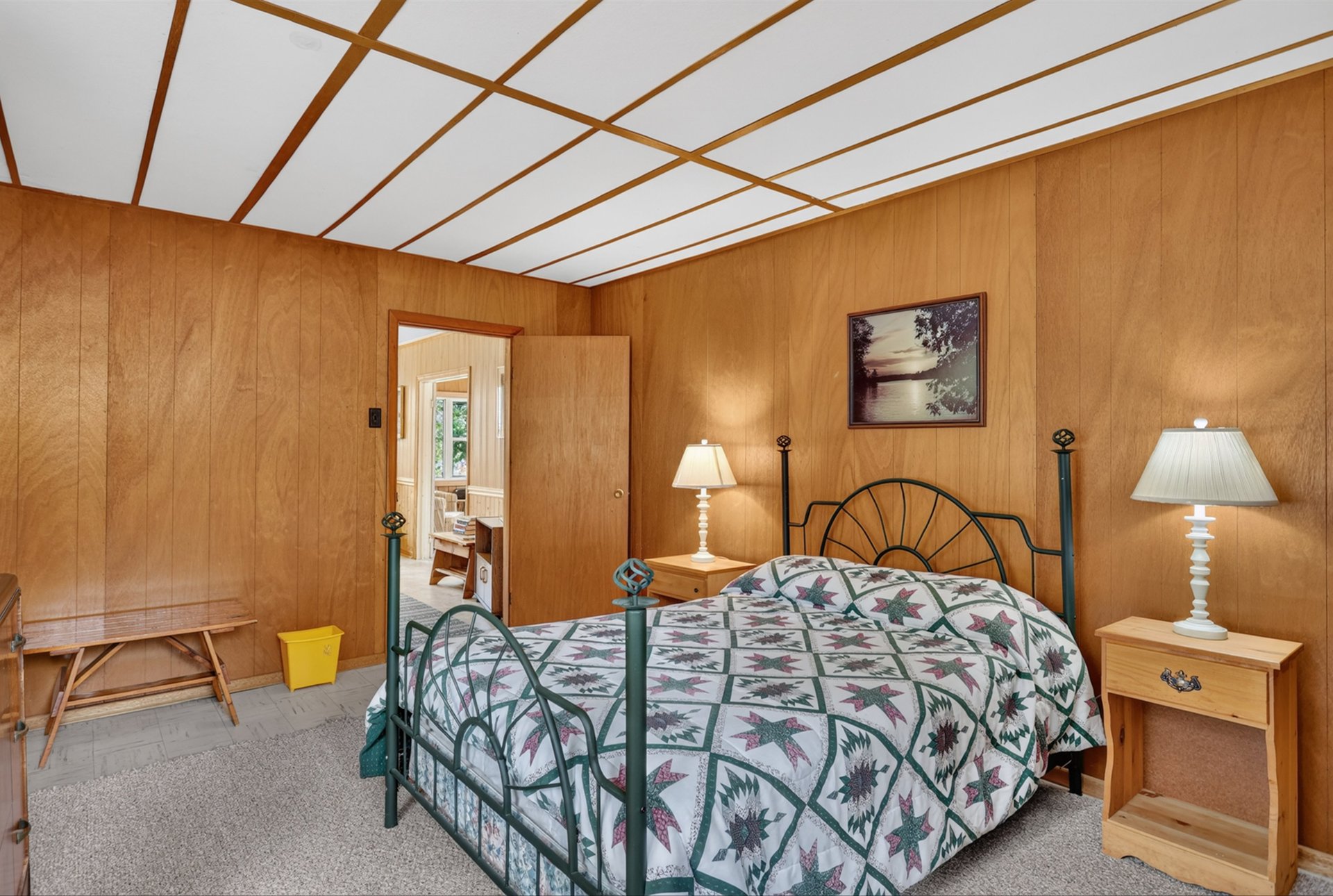 Bedroom with wood-paneled walls, a metal four-poster bed, and a patterned quilt.
