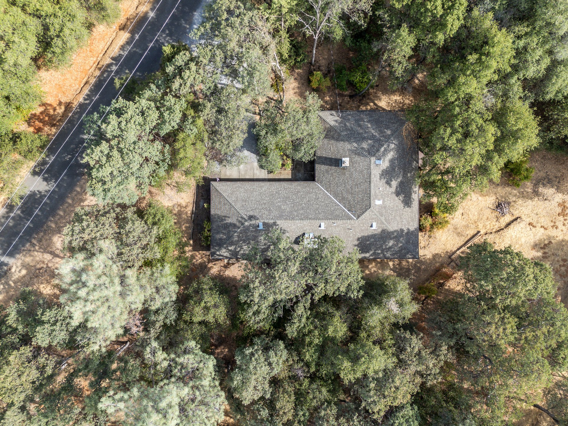 Aerial view of a gray-shingled house nestled among trees beside a road.