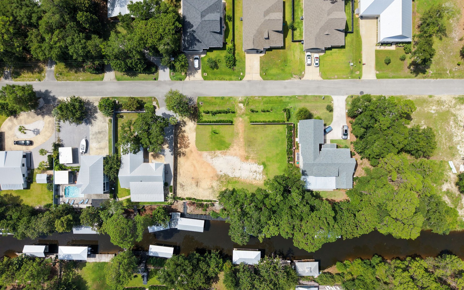 Aerial view of waterfront homes and cleared lots beside a canal.
