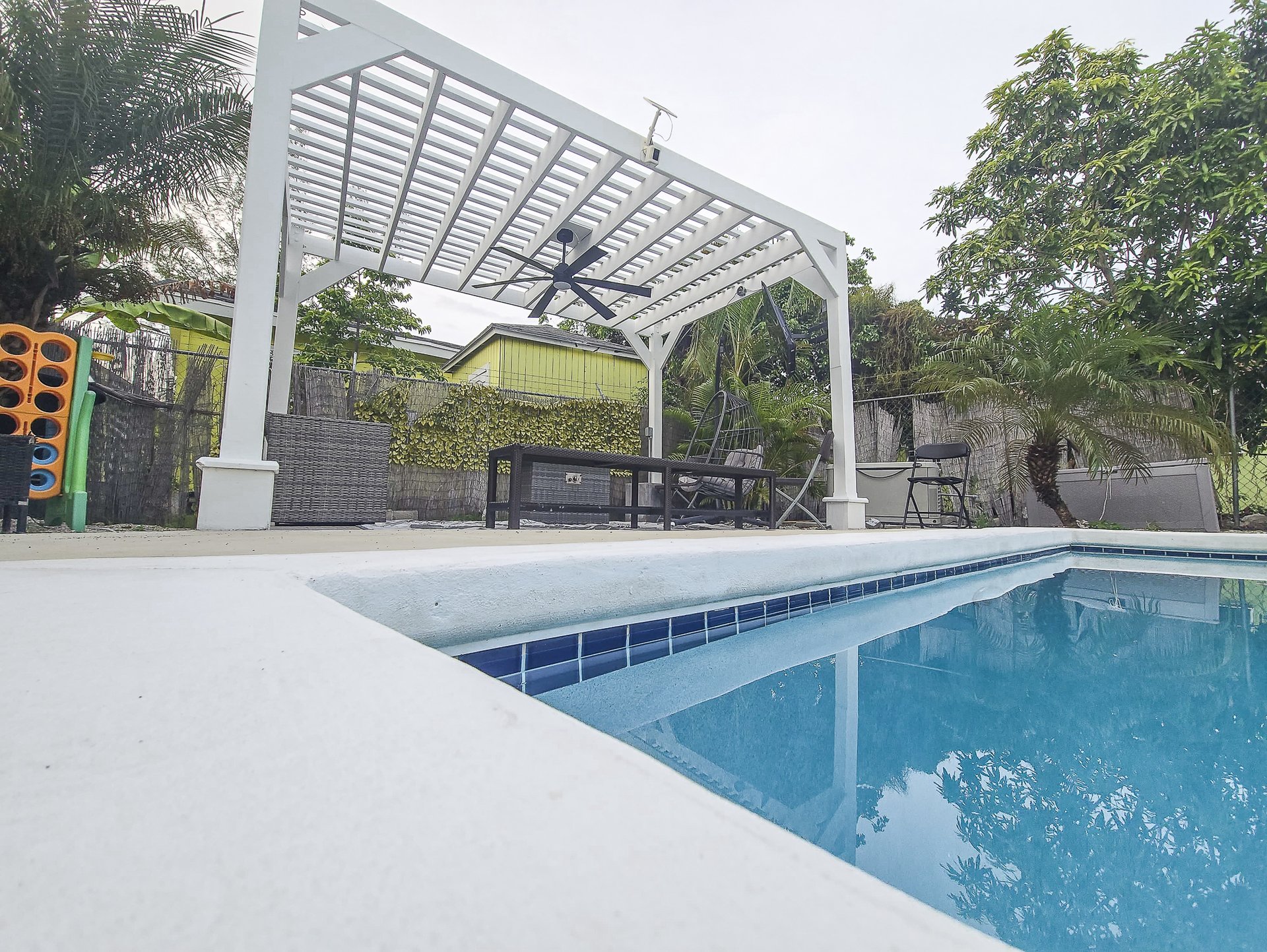 Swimming pool beside a white pergola-covered patio with outdoor seating.
