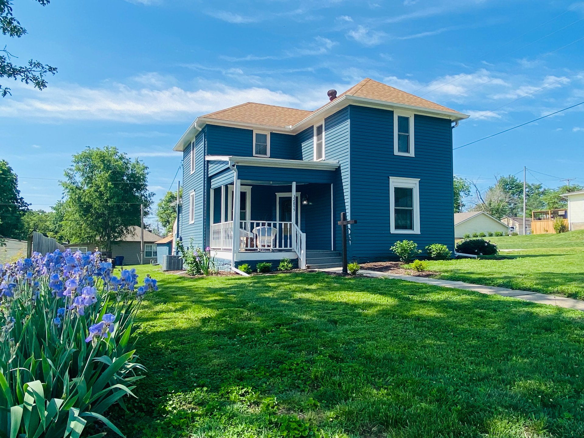 Two-story blue house with a covered porch and purple irises in the front yard.