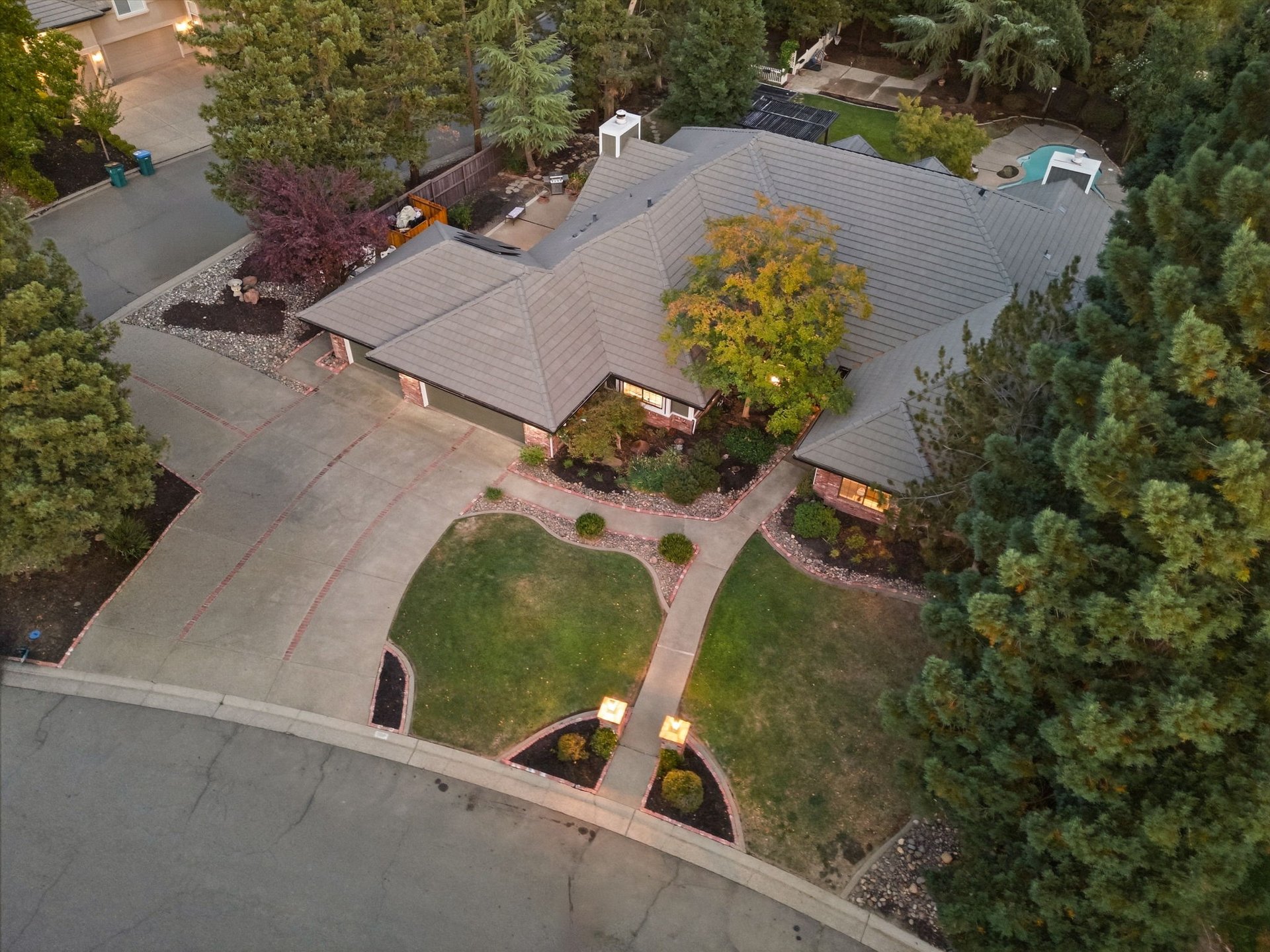 Aerial view of a home with a broad gray tile roof, landscaped yard, and large paved driveway.
