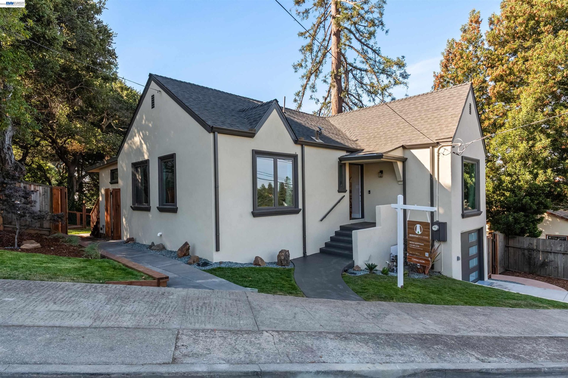 Light stucco house with dark gabled roofs, front steps, landscaped lawn, and attached garage.