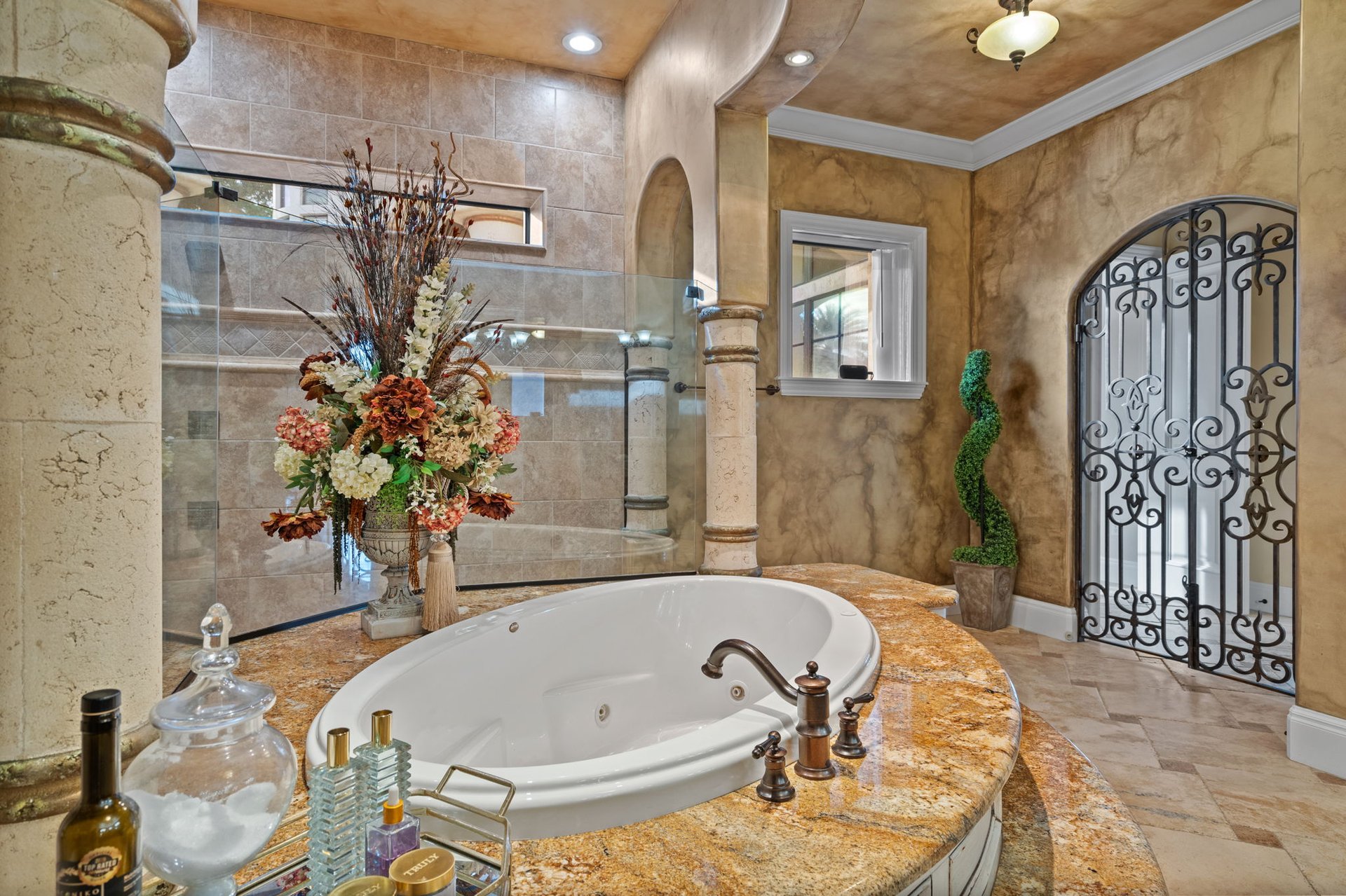 Ornate bathroom with an oval soaking tub, glass shower, and wrought-iron arched doorway.